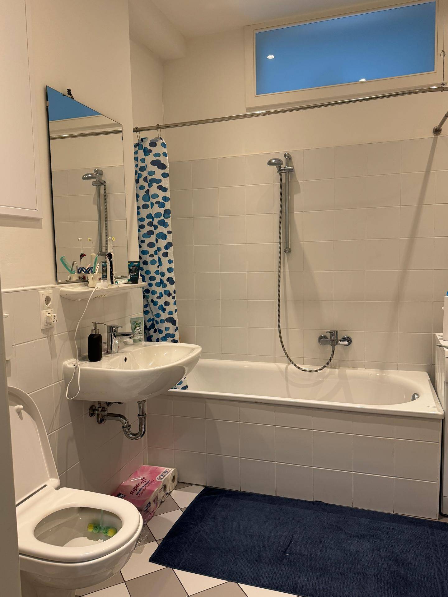 Badezimmer mit Badewanne, integrierter Dusche, WC und einem kleinen Fenster für Belüftung.