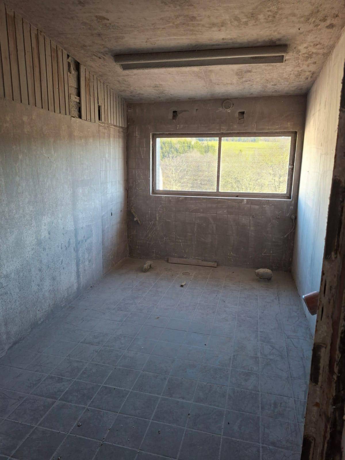 Unfertiger Raum mit Betonwänden, Fliesenboden und einem Fenster, das auf eine grüne Landschaft blickt.