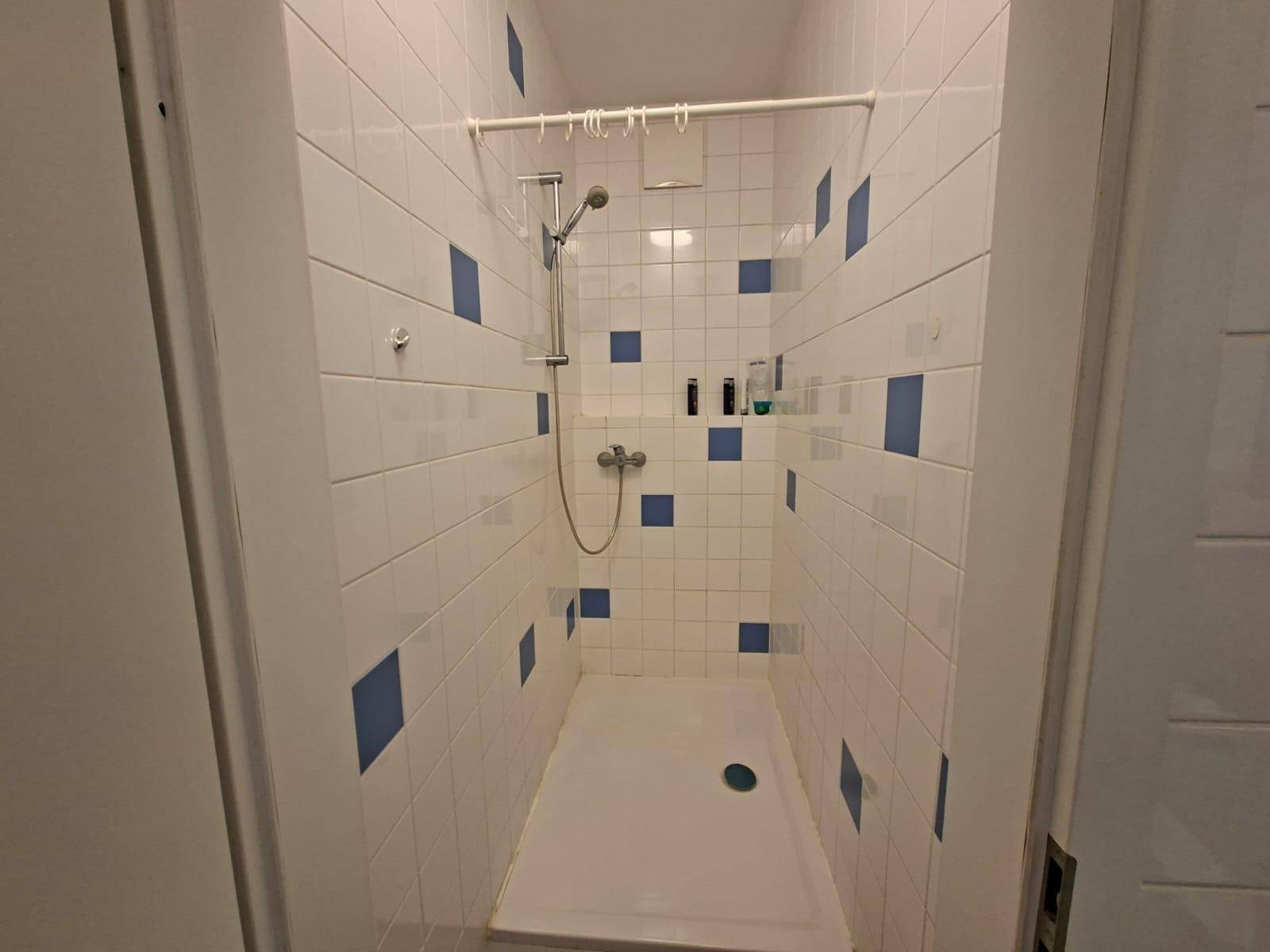Geflieste Duschkabine mit weißen und blauen Fliesen, ausgestattet mit einer einfachen Duscharmatur.