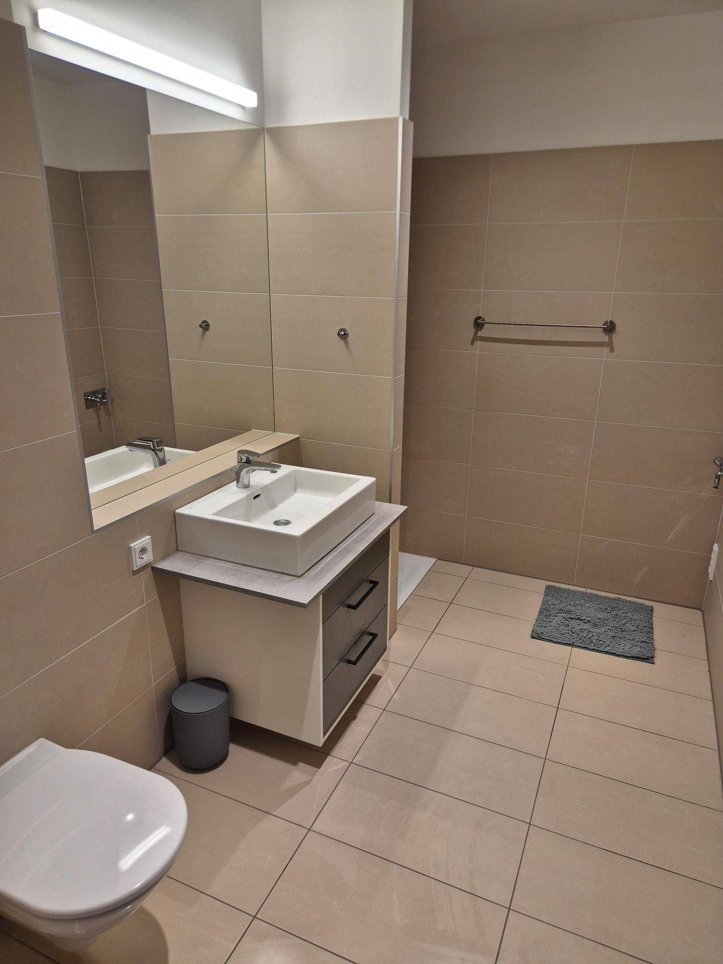 Modernes Badezimmer mit beigen Fliesen, wandhängendem WC und Aufsatzwaschbecken.