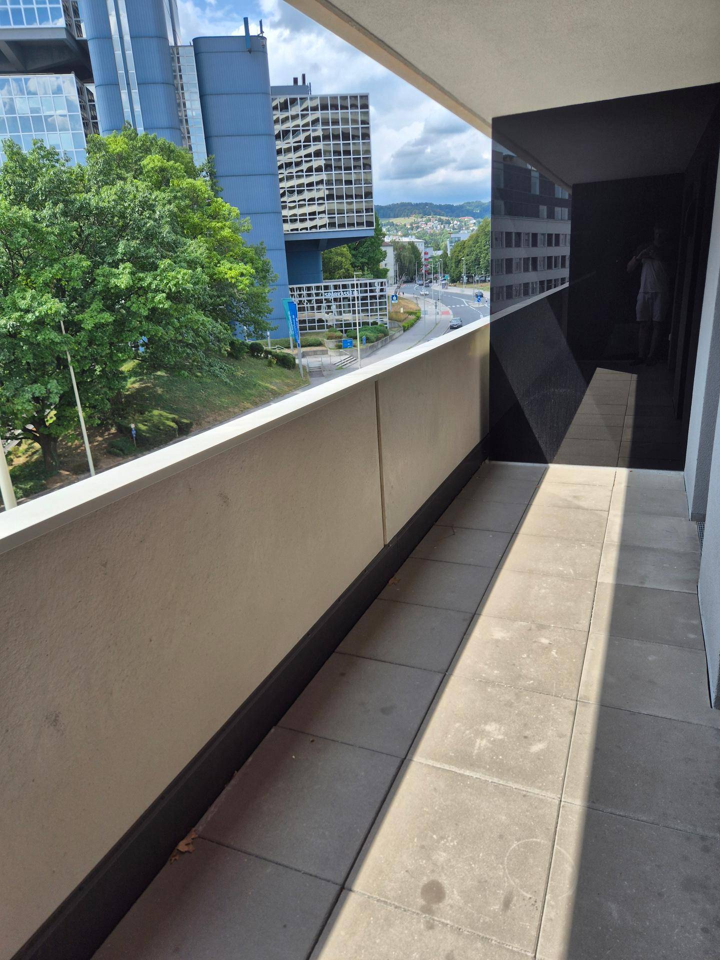 Langer Balkon mit Fliesenboden und urbanem Ausblick auf die Stadt und Bäume.