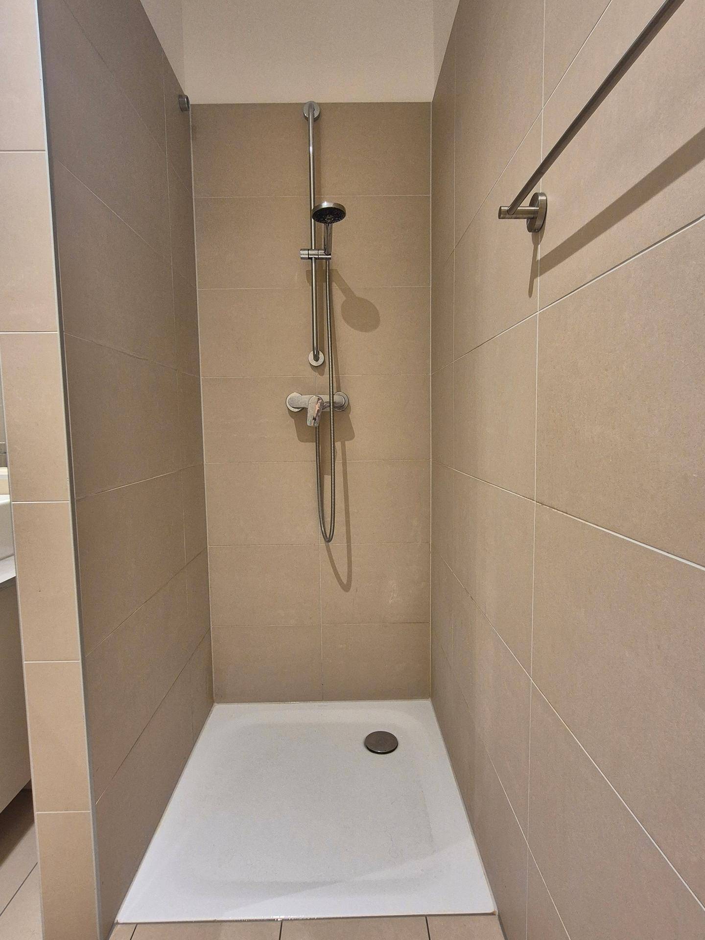 Geräumige, begehbare Dusche mit beigen Fliesen und moderner Duscharmatur.