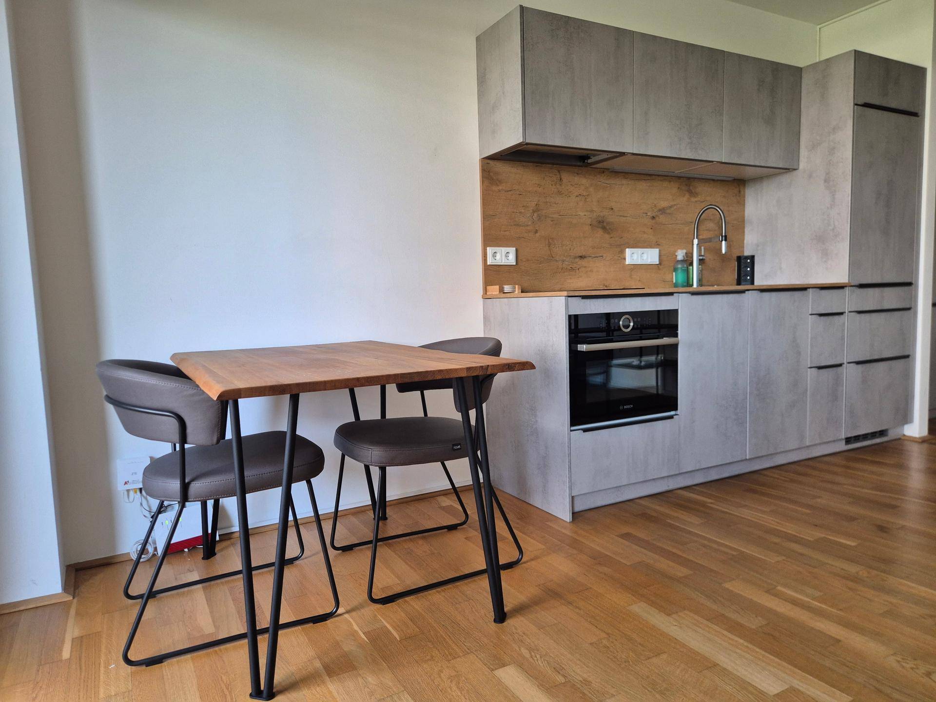 Moderne Einbauküche mit grauen Fronten, Holzakzenten und integriertem Essbereich.