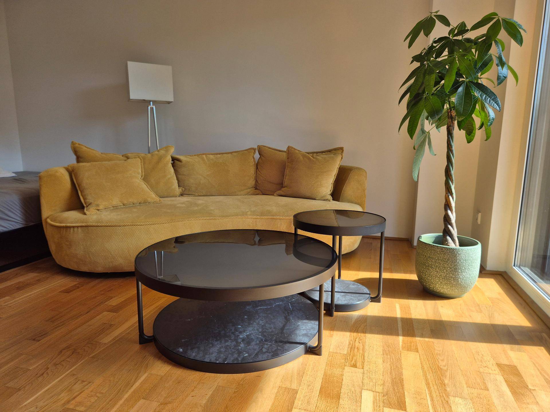 Gemütliches Wohnzimmer mit beigem Sofa, modernen Couchtischen und viel Tageslicht.