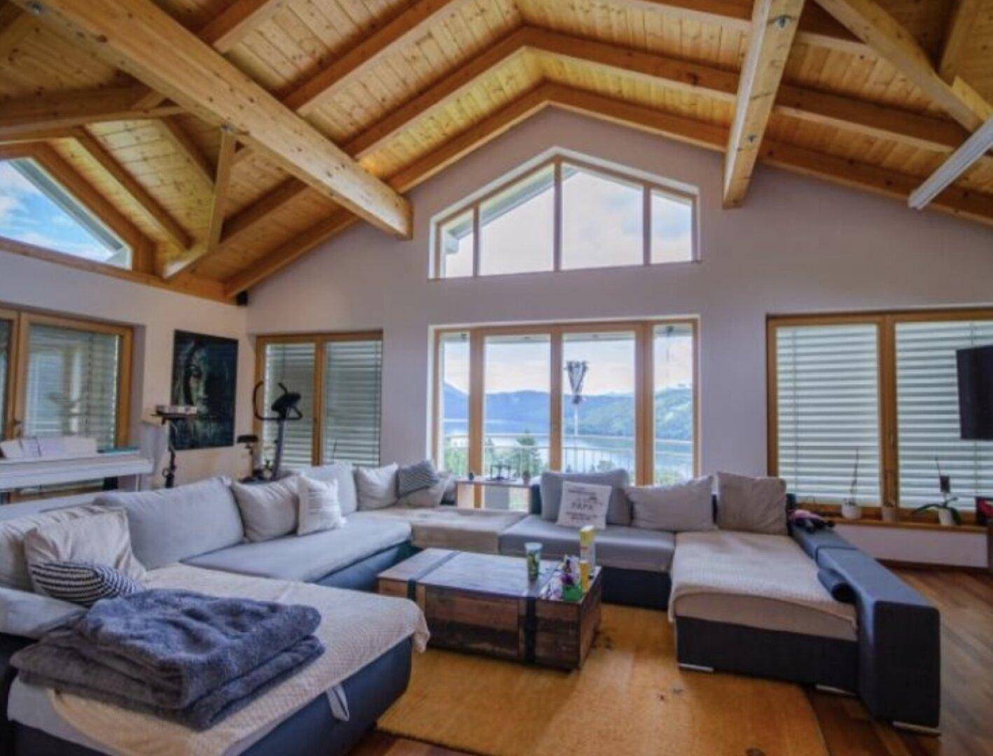 Gemütlich eingerichtetes Wohnzimmer mit großer Sofalandschaft, Holzbalkendecke und Seeblick.