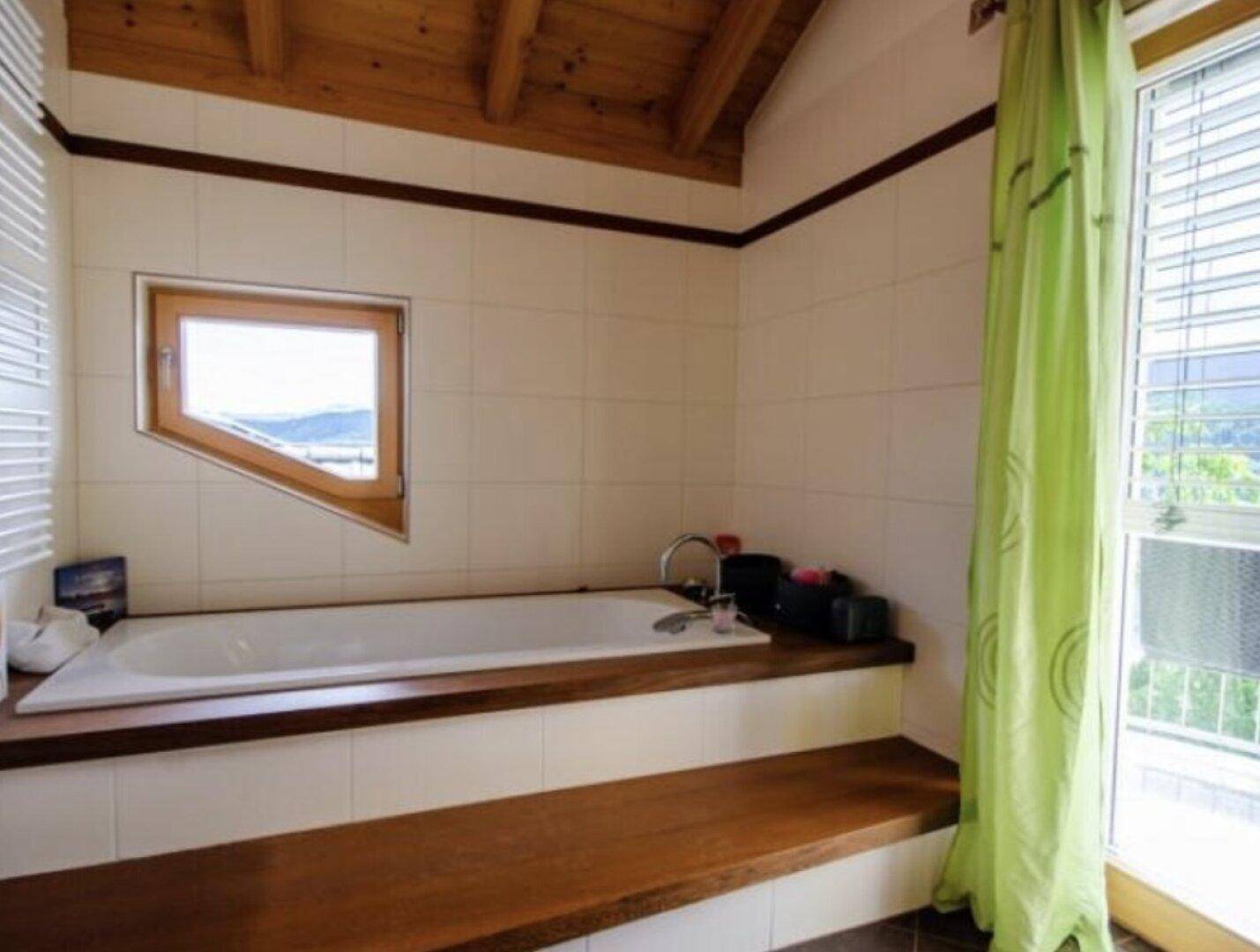 Badezimmer mit Badewanne, Holzverkleidung und einem schrägen Fenster mit Ausblick.