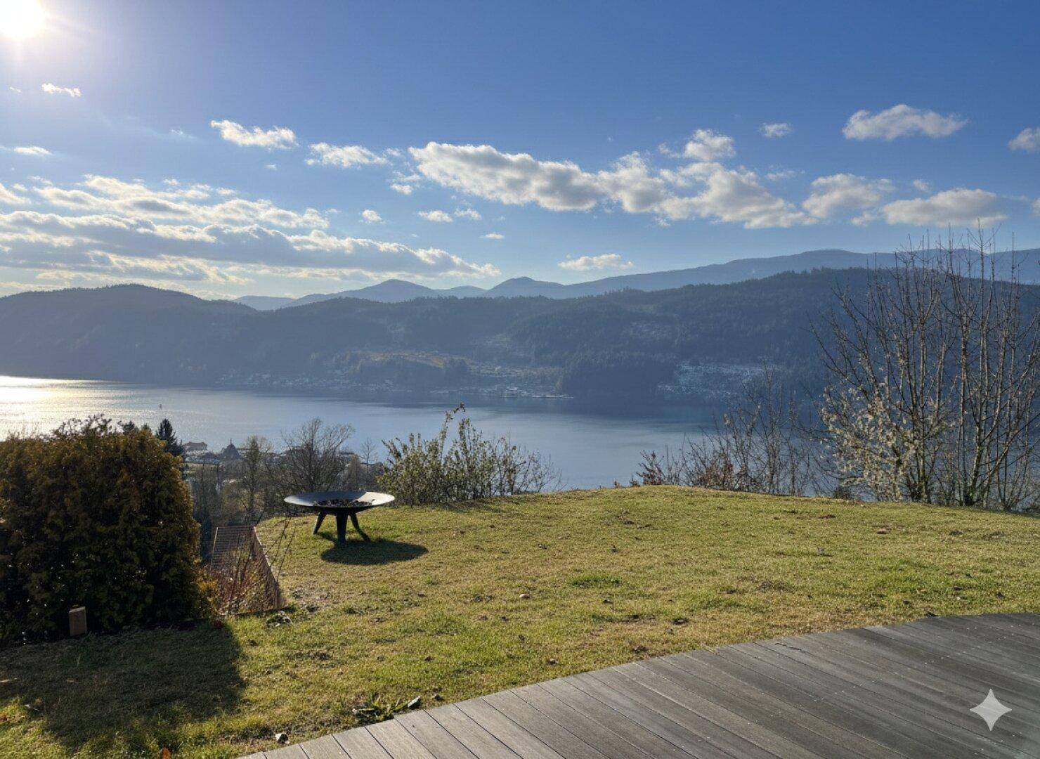 Sonnige Terrasse mit Holzboden und weitem Blick auf den See und die umliegenden Berge.