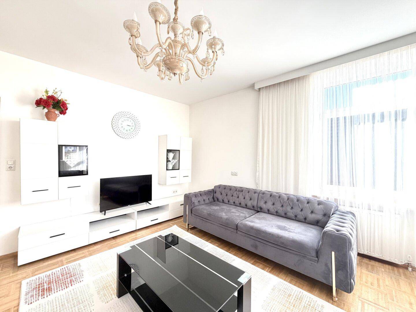 Helles Wohnzimmer mit modernem Sofa, weißer Schrankwand und Kronleuchter.