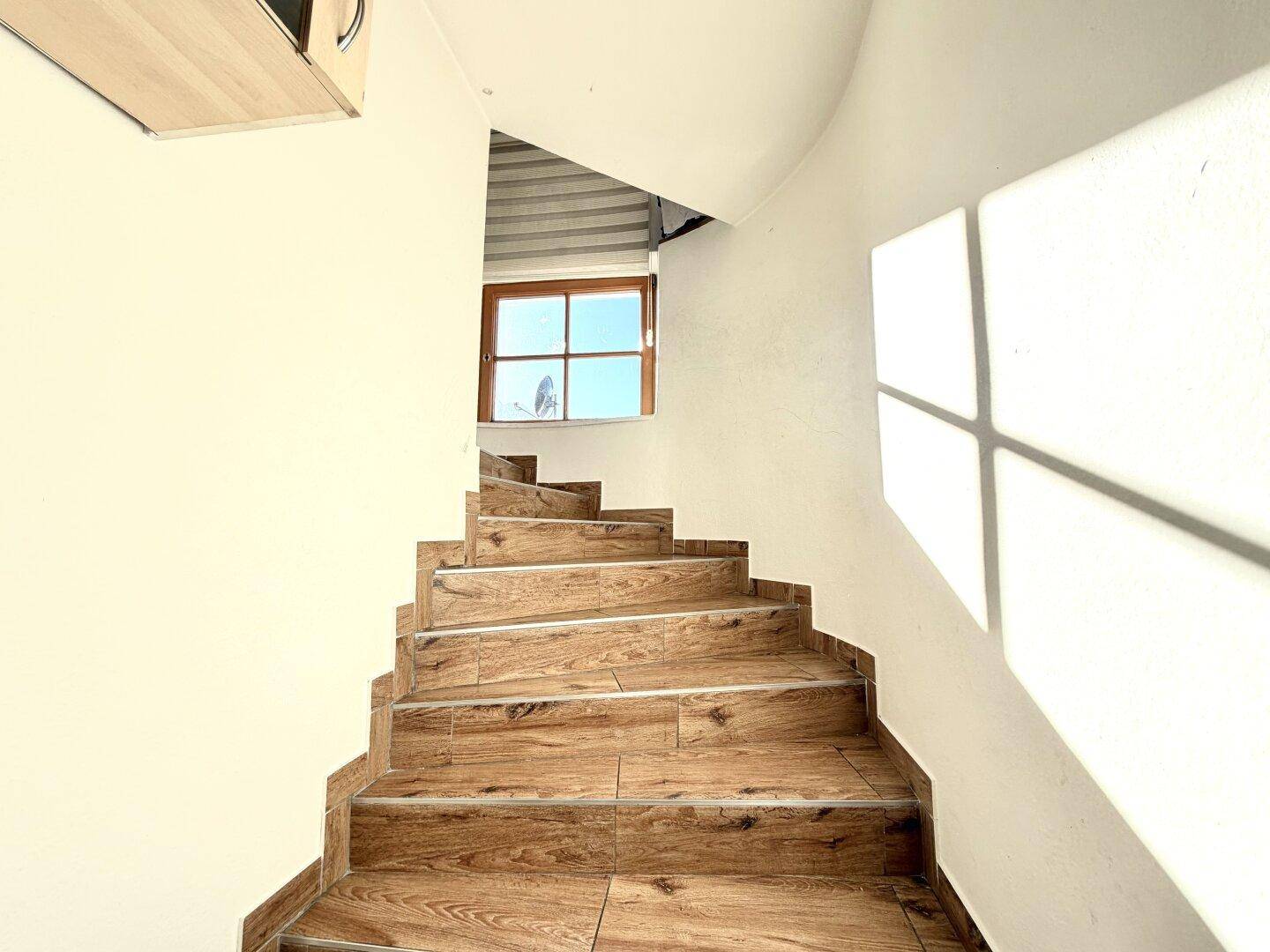 Helle Treppe mit Holzoptikfliesen und Fenster, das viel Tageslicht hereinlässt.