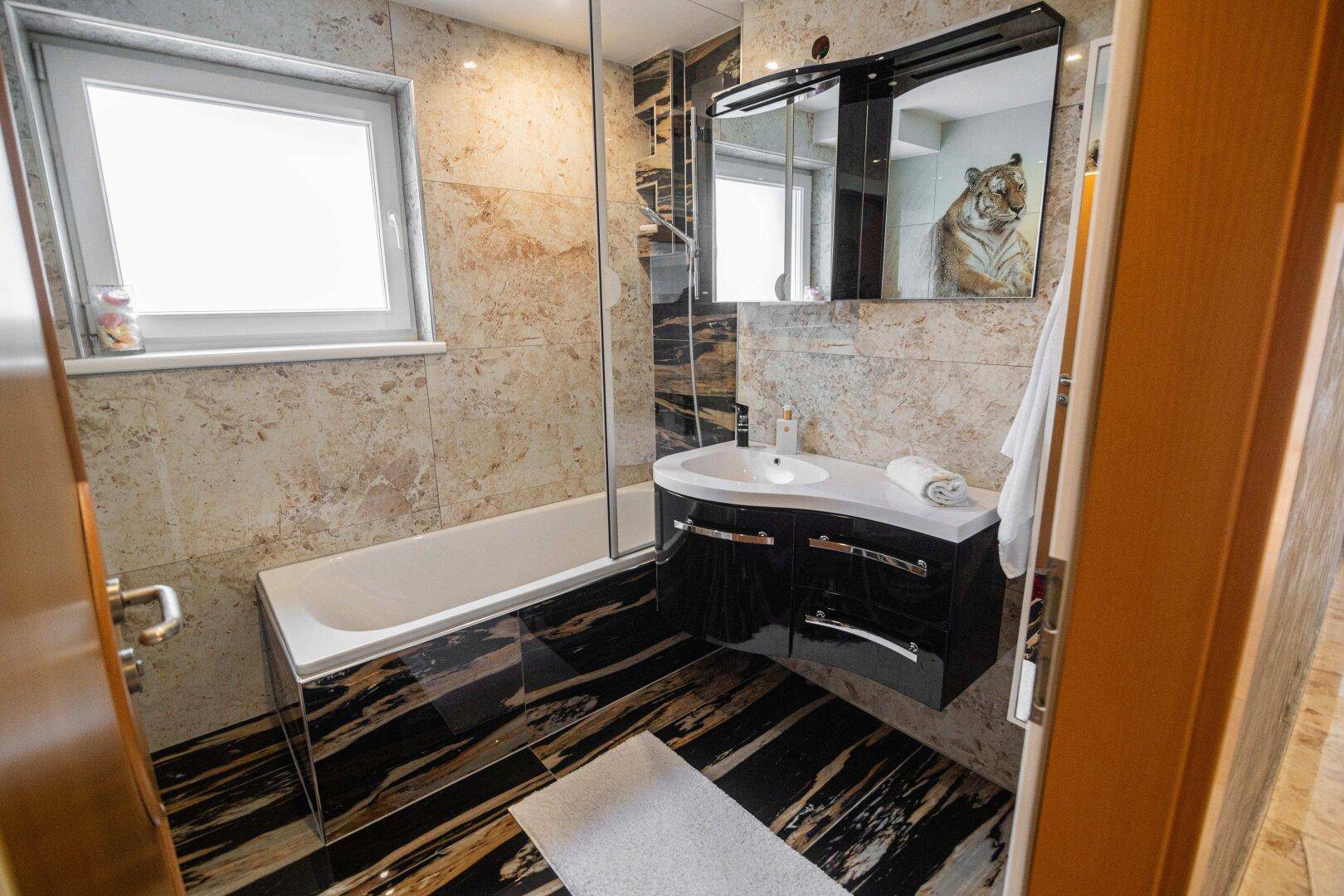 Modernes Badezimmer mit Badewanne, Waschbecken, Spiegelschrank und eleganten Marmorfliesen.