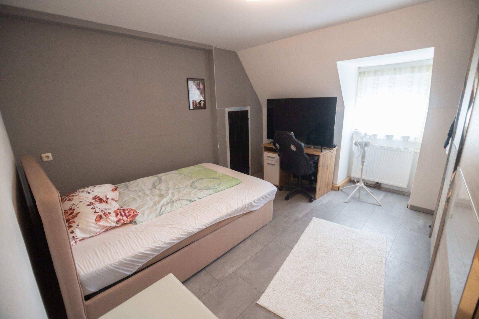 Gemütliches Schlafzimmer mit Einzelbett, Schreibtisch und Fernseher unter einer Dachschräge.