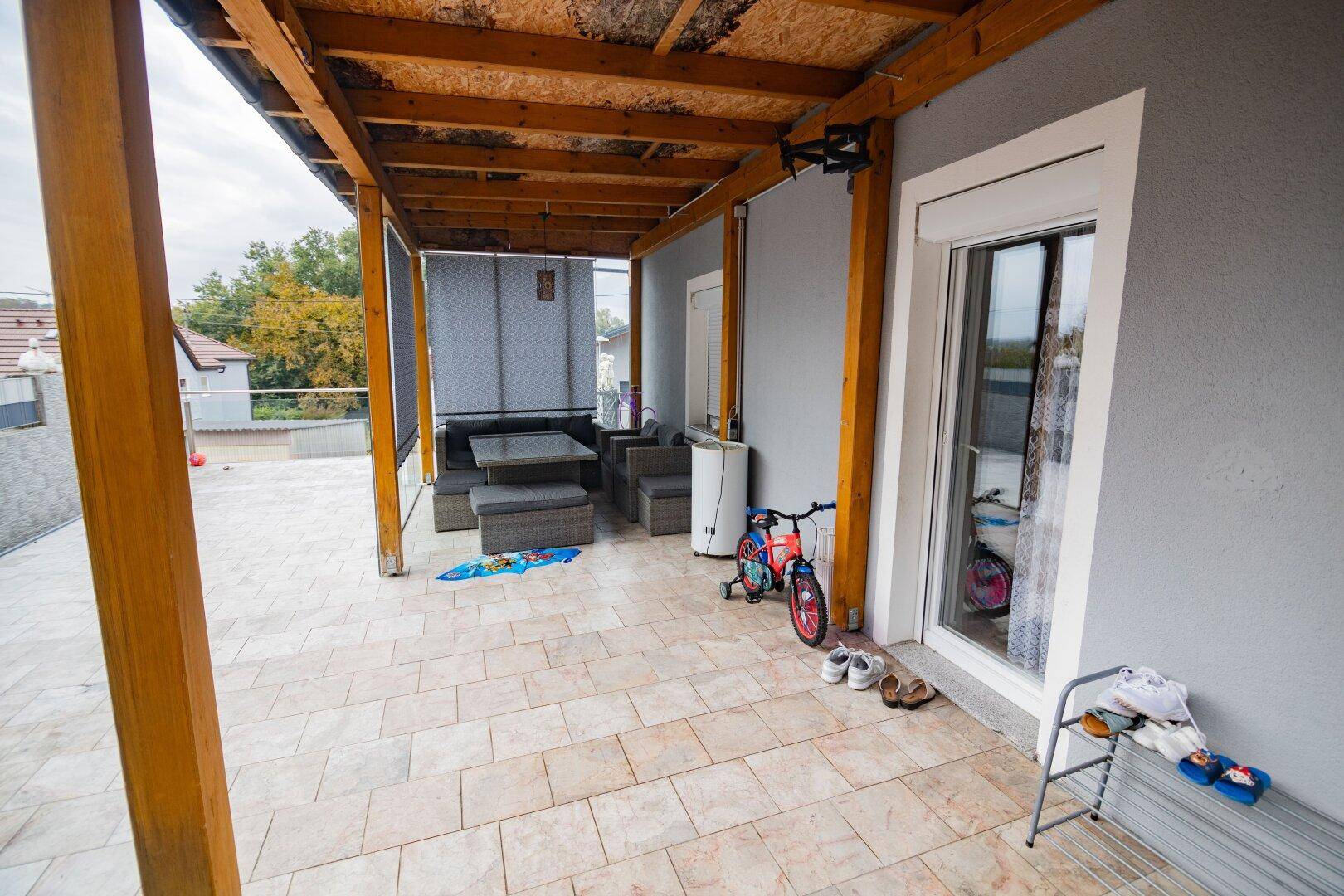 Überdachte Terrasse mit Sitzgelegenheiten und Fliesenboden, ideal für entspannte Stunden im Freien.