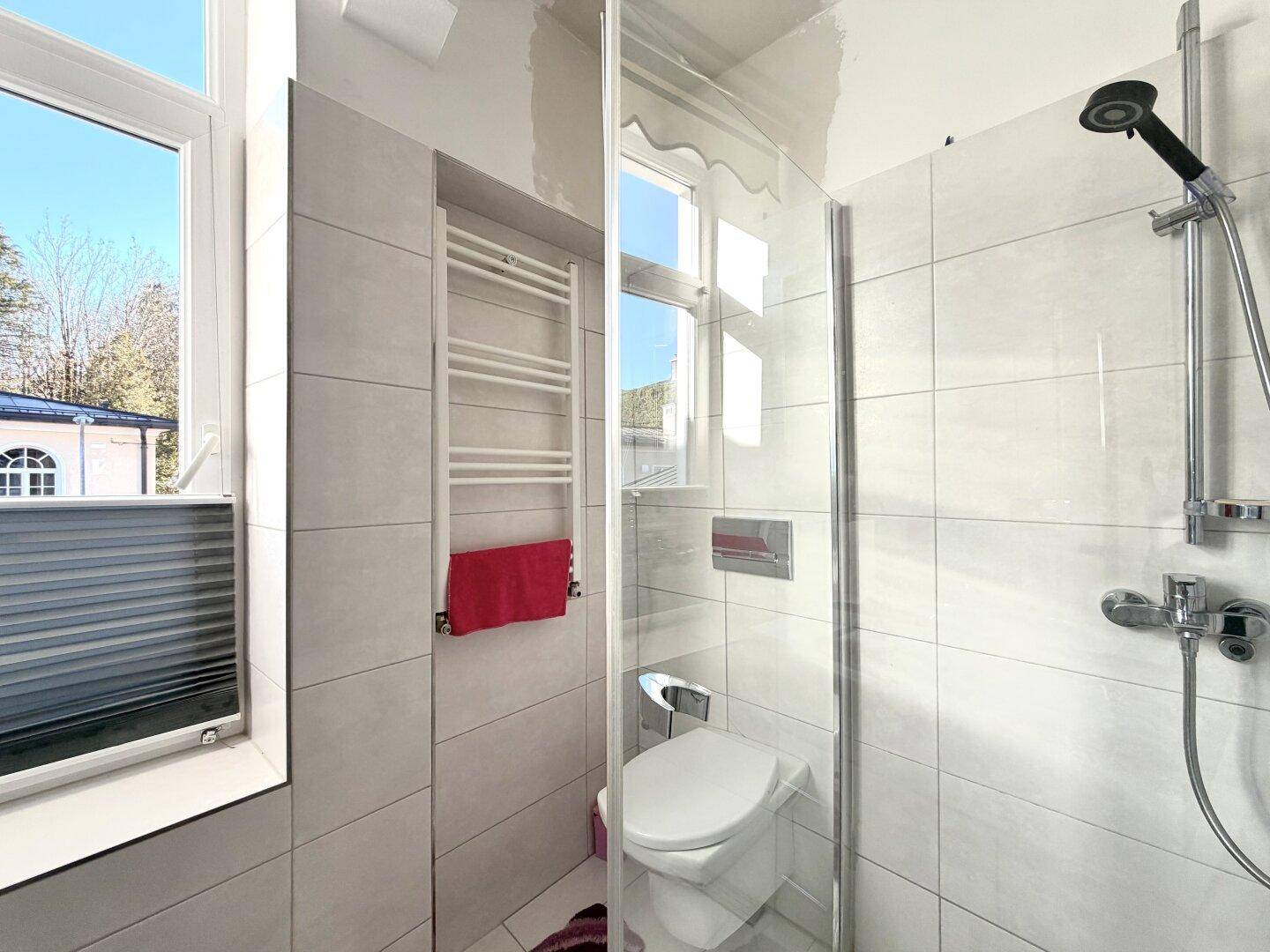 Modernes Badezimmer mit Duschkabine, wandhängendem WC und beheiztem Handtuchhalter.