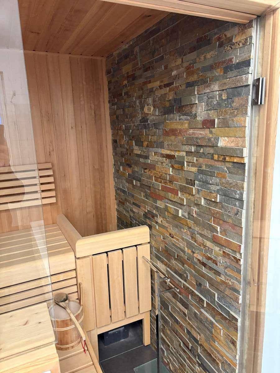 Eingangsbereich der Sauna mit Holzbänken, Steinwand und Saunaofen.