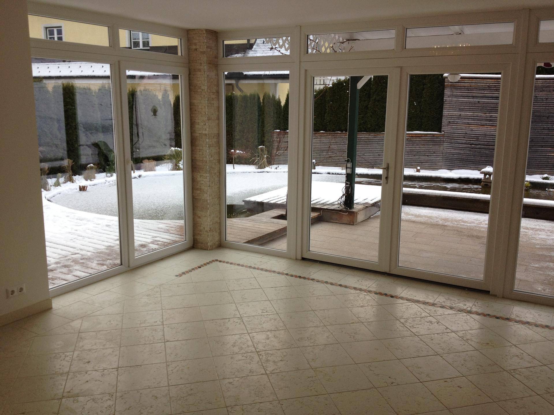 Heller Wintergarten mit großen Glasfronten und Blick auf den verschneiten Garten.