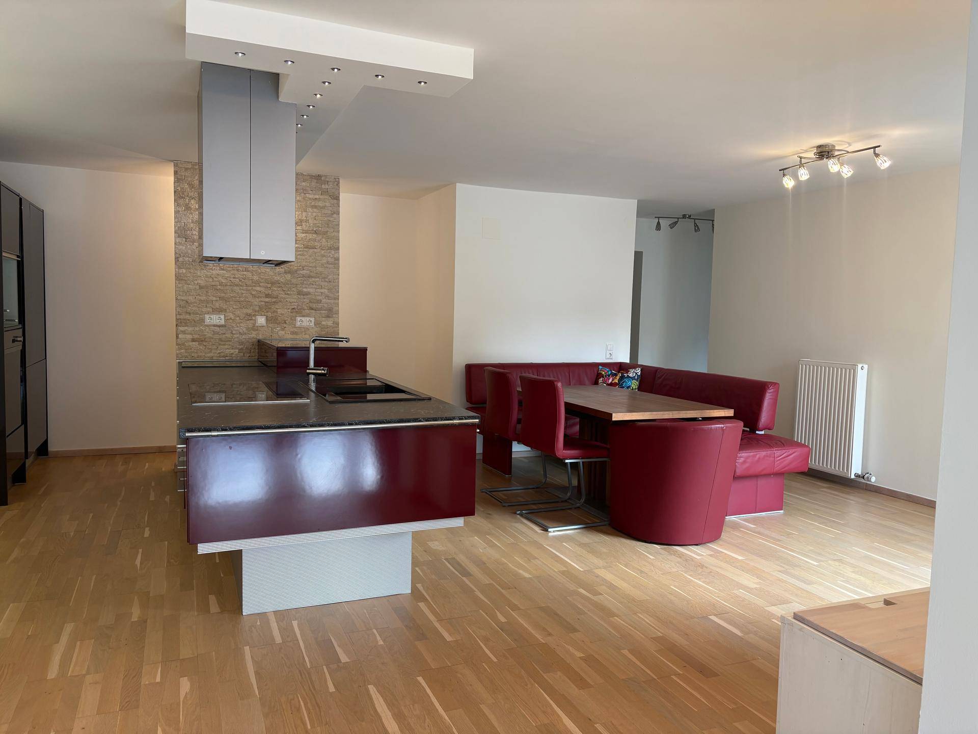 Geräumiger offener Wohn-Essbereich mit moderner Küche, Holzboden und roter Eckbank.