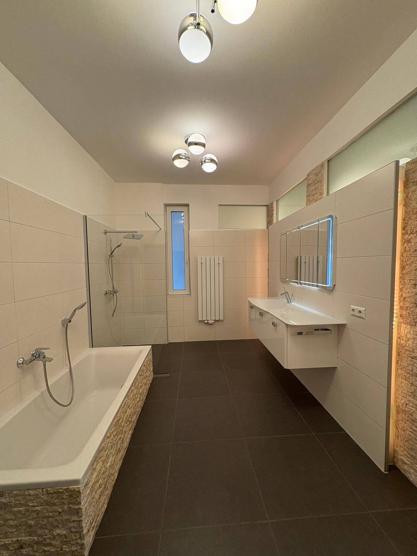 Geräumiges Badezimmer mit Badewanne, Duschbereich und großem Waschtisch mit Spiegelschrank.