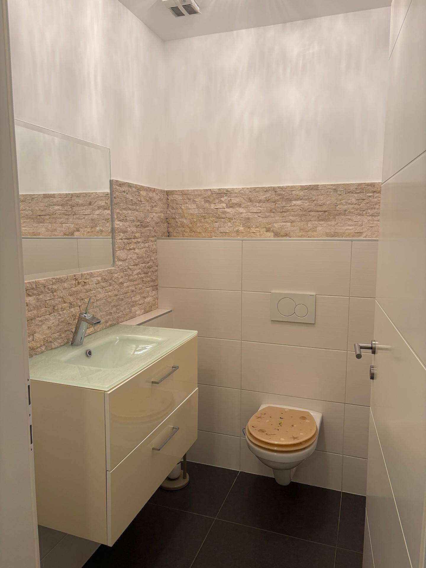 Kleines Gäste-WC mit modernem Waschtisch, Wand-WC und dekorativer Steinwand.