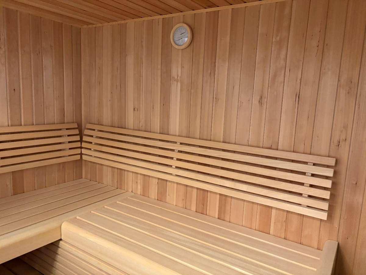 Innenansicht einer Holzsauna mit mehreren Sitzebenen und einer Wanduhr.