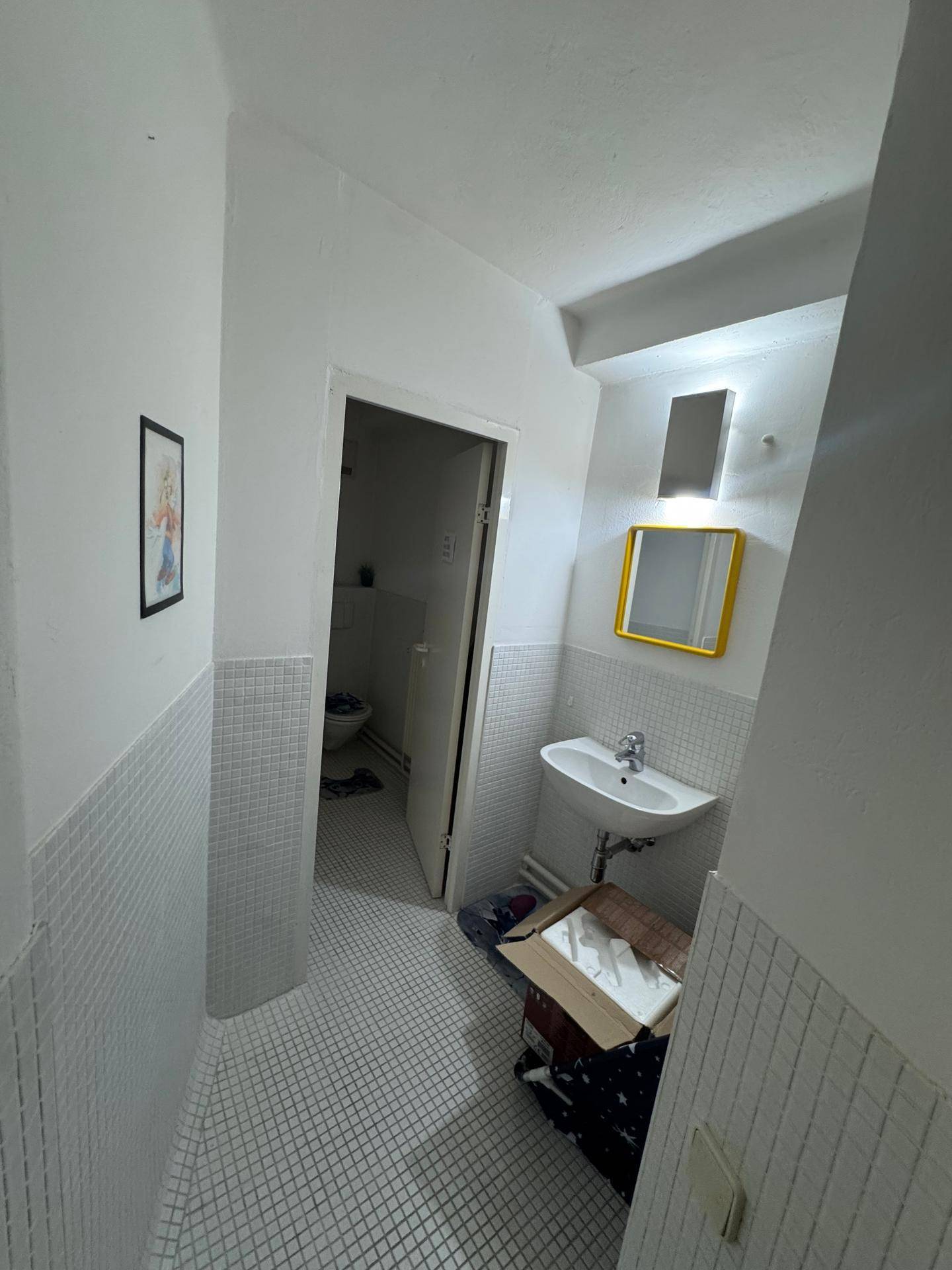 Badezimmer mit weißen Fliesen, Waschbecken und einem Spiegel mit gelbem Rahmen.