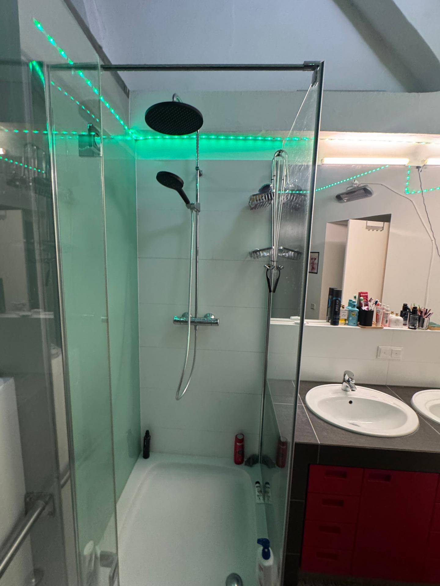 Modernes Badezimmer mit Glasdusche, Regendusche und Doppelwaschbecken mit roten Akzenten.