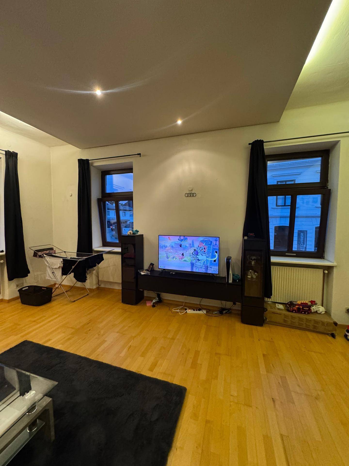 Heller Wohnbereich mit Parkettboden, Fenstern und einem Fernseher.