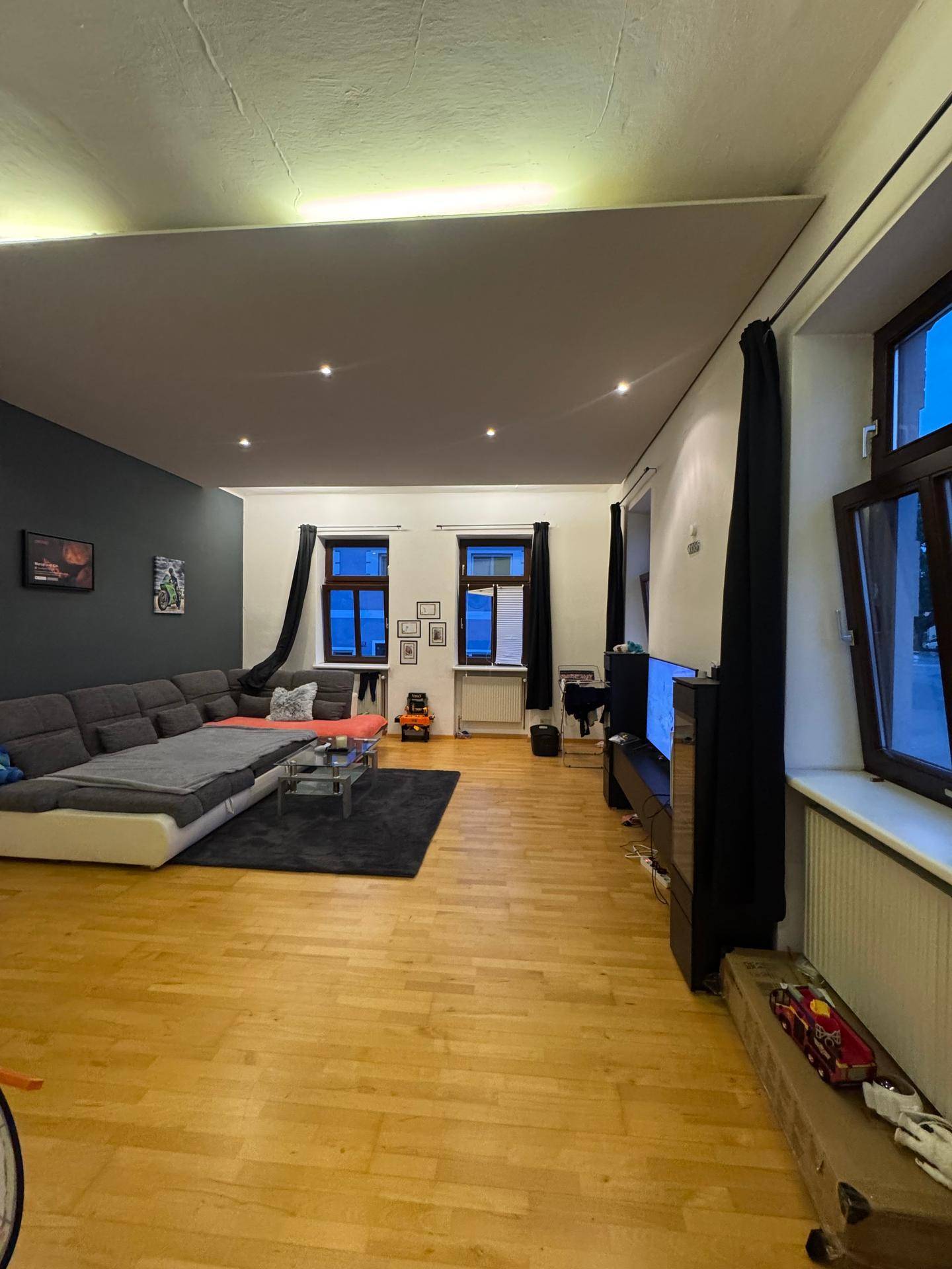 Geräumiges Wohnzimmer mit Parkettboden, großem Sofa und Fernseher.