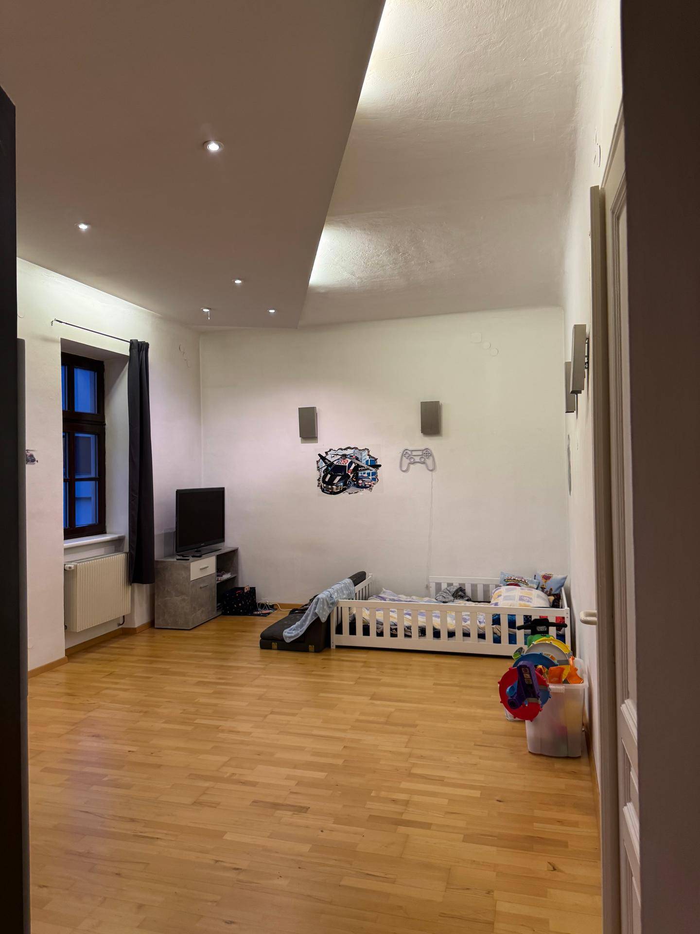 Kinderzimmer mit Parkettboden, Fenstern und Spielzeug.