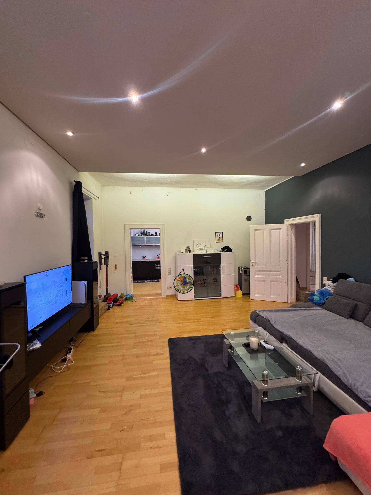Weitläufiges Wohnzimmer mit Parkettboden und Blick auf die angrenzende Küche.