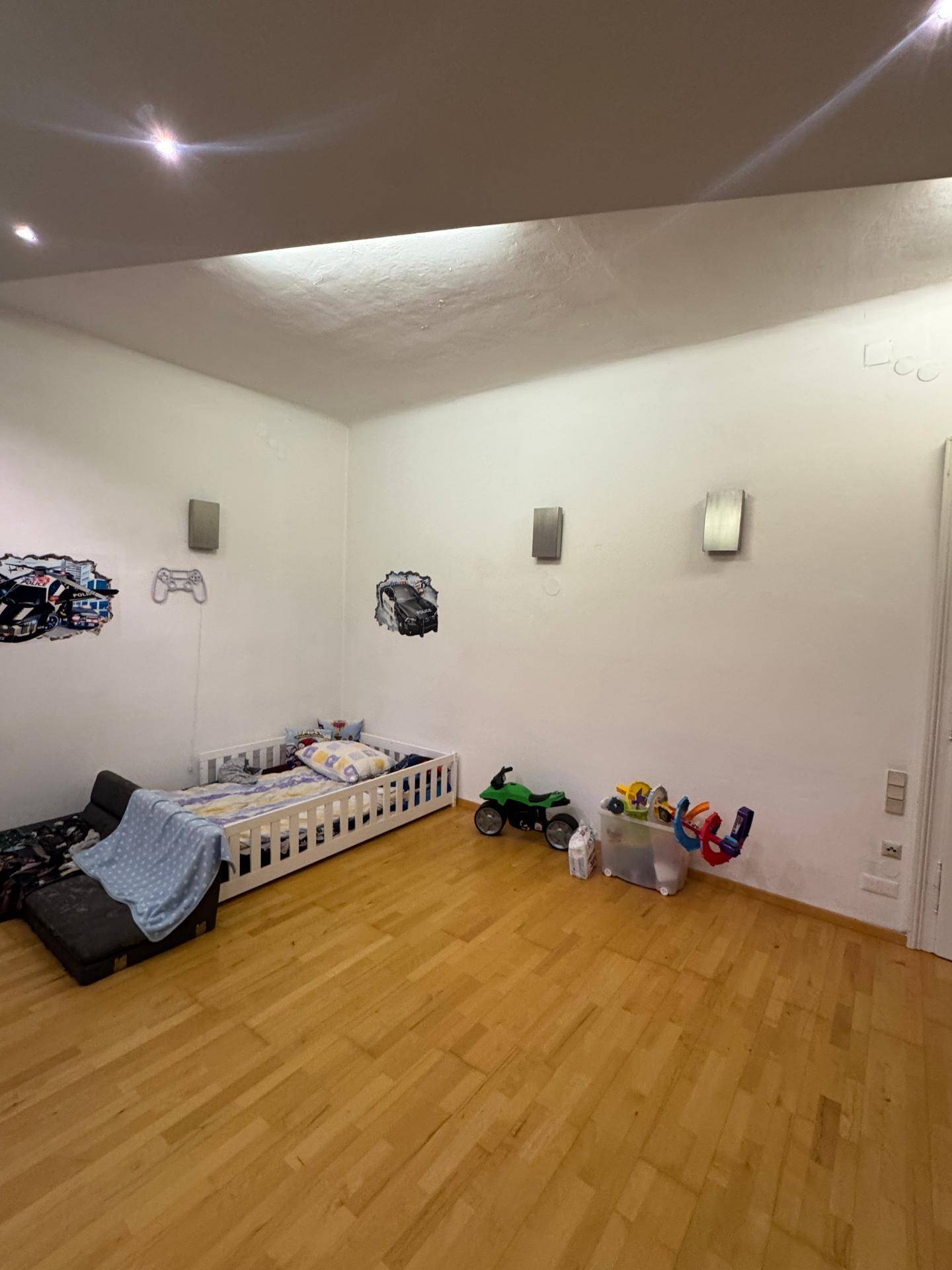 Kinderzimmer mit niedrigem Bett, Spielzeug und Wanddekorationen auf hellem Holzfußboden.