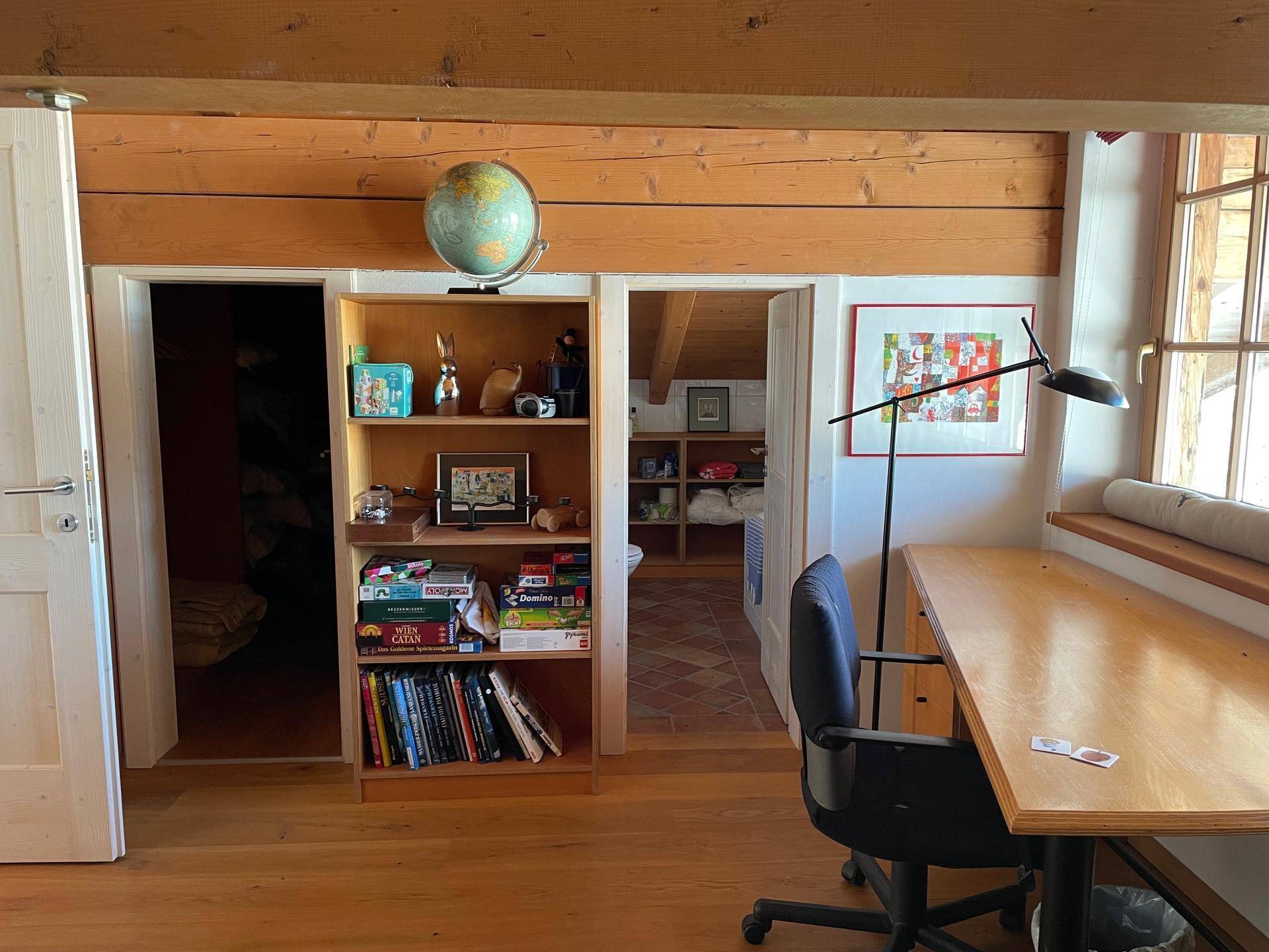Dachgeschoss-Arbeitsbereich mit Holzbalken, Schreibtisch und Regalen.