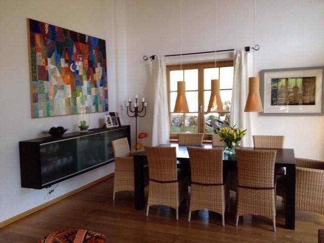 Heller Essbereich mit Holztisch, Korbstühlen und einem großen Fenster mit Blick nach draußen.