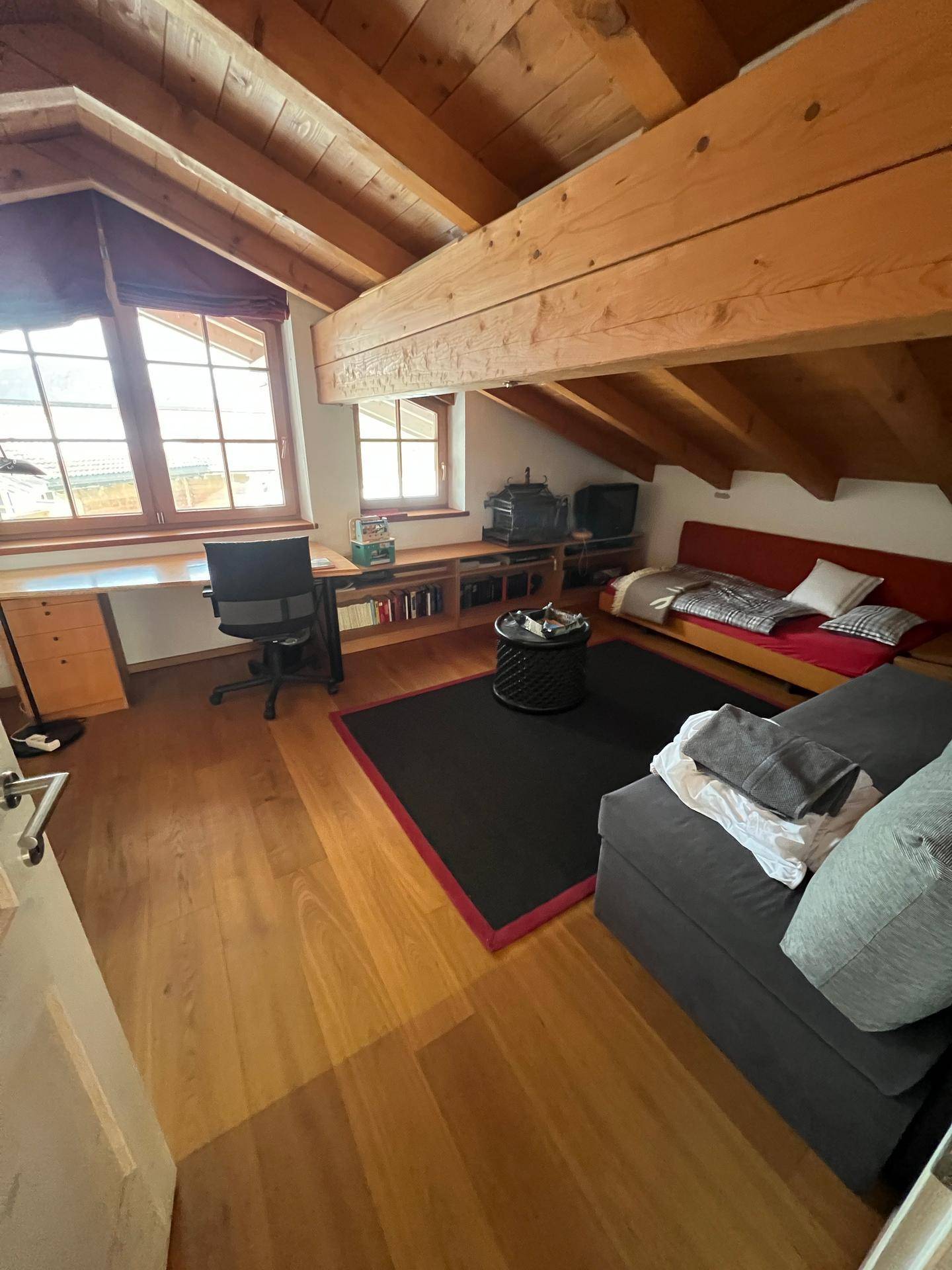 Gemütlicher Dachgeschossraum mit Holzbalken, Sofa und Arbeitsbereich.