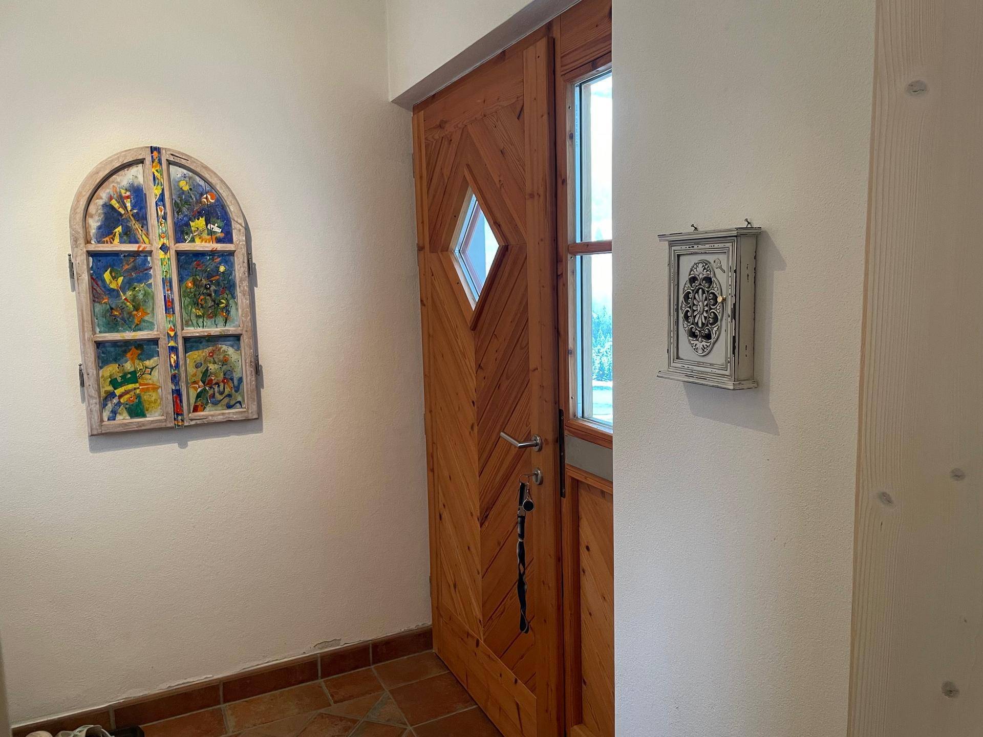 Eingangsbereich mit Holztür und Terrakotta-Boden, geschmückt mit einem bunten Fensterbild.