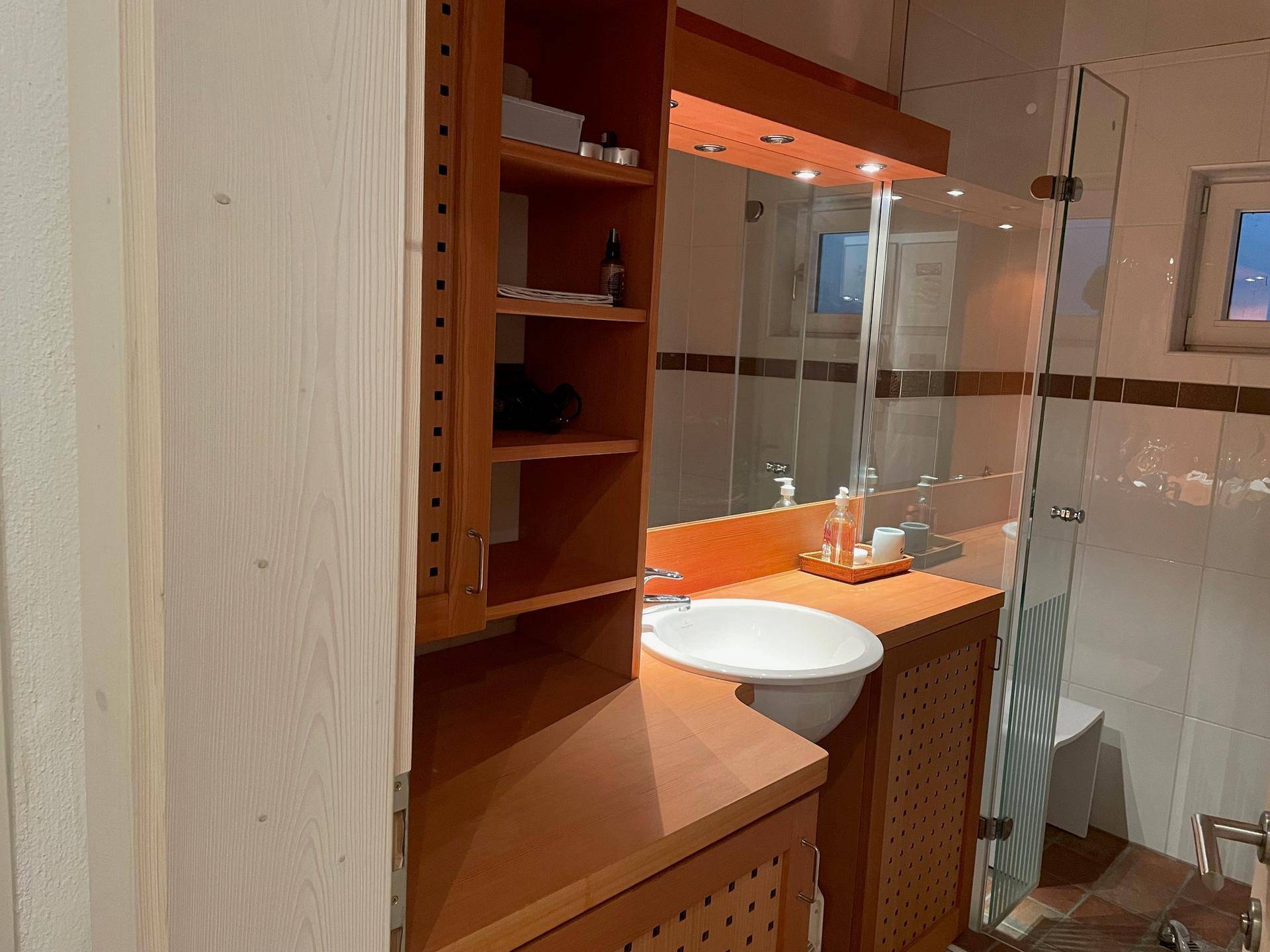 Badezimmer mit Holzwaschtisch, Spiegel und Duschkabine.