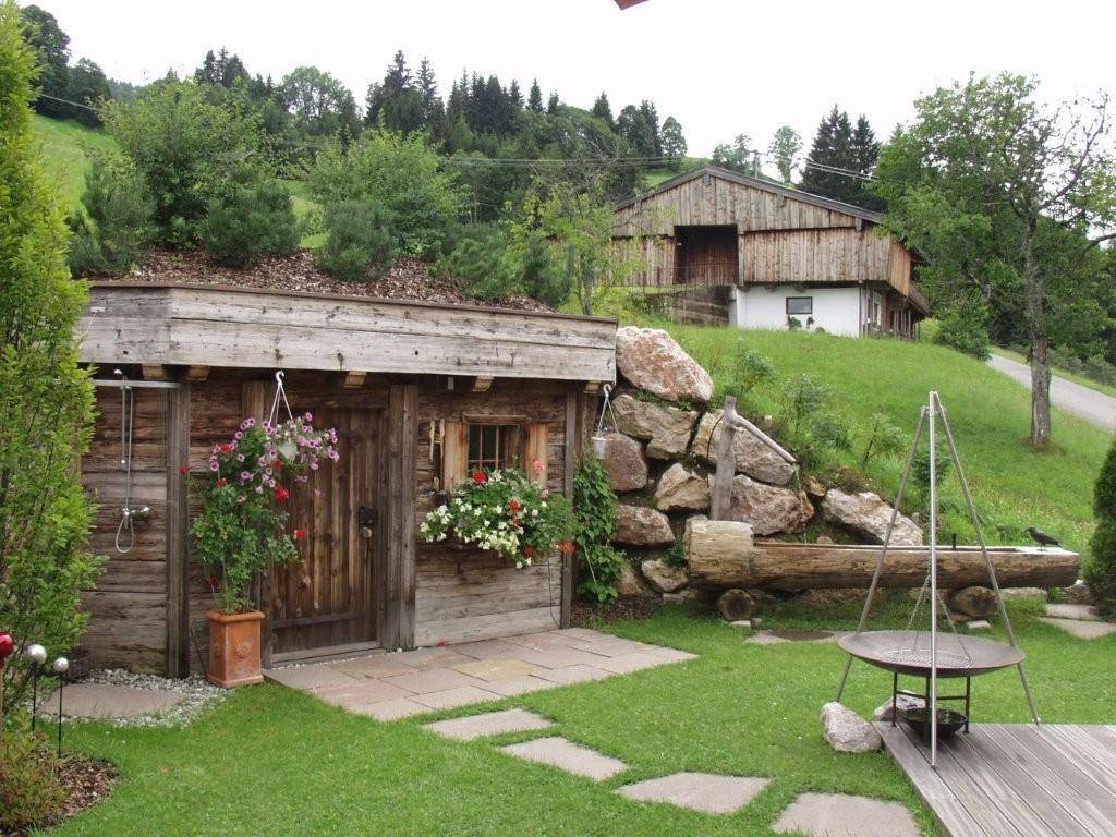 Rustikaler Gartenbereich mit Holzhütte, Grillstelle und Blick auf die bewaldeten Hügel.