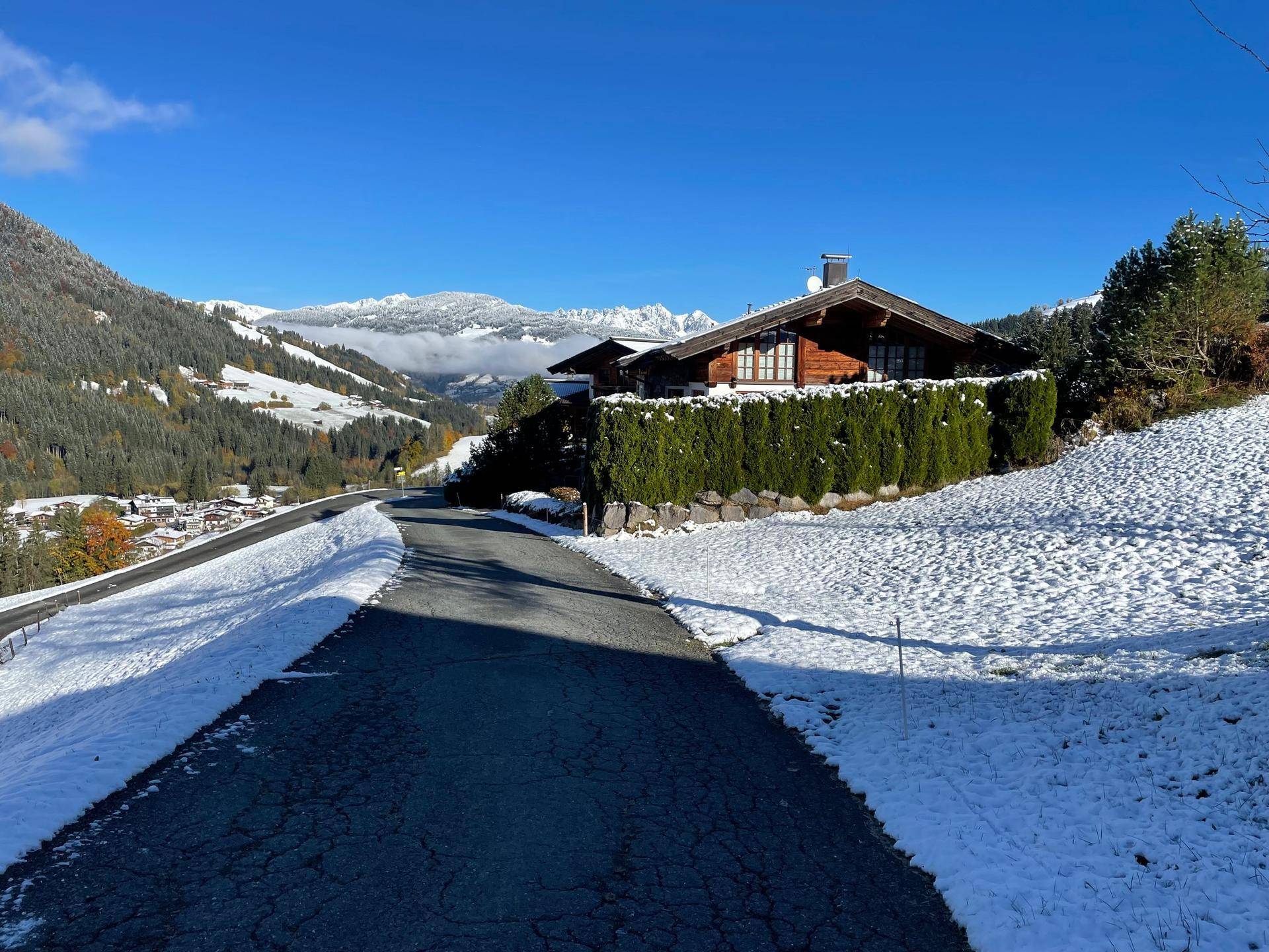 Anwesen in alpiner Umgebung mit verschneiter Straße und grüner Hecke.
