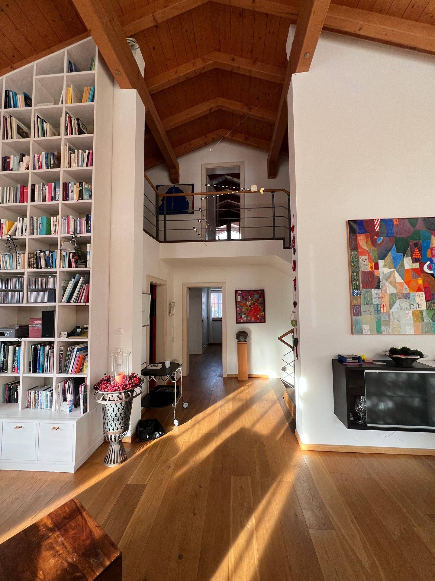 Heller Eingangsbereich mit hoher Decke, Holzbalken und einer großen Bücherwand.
