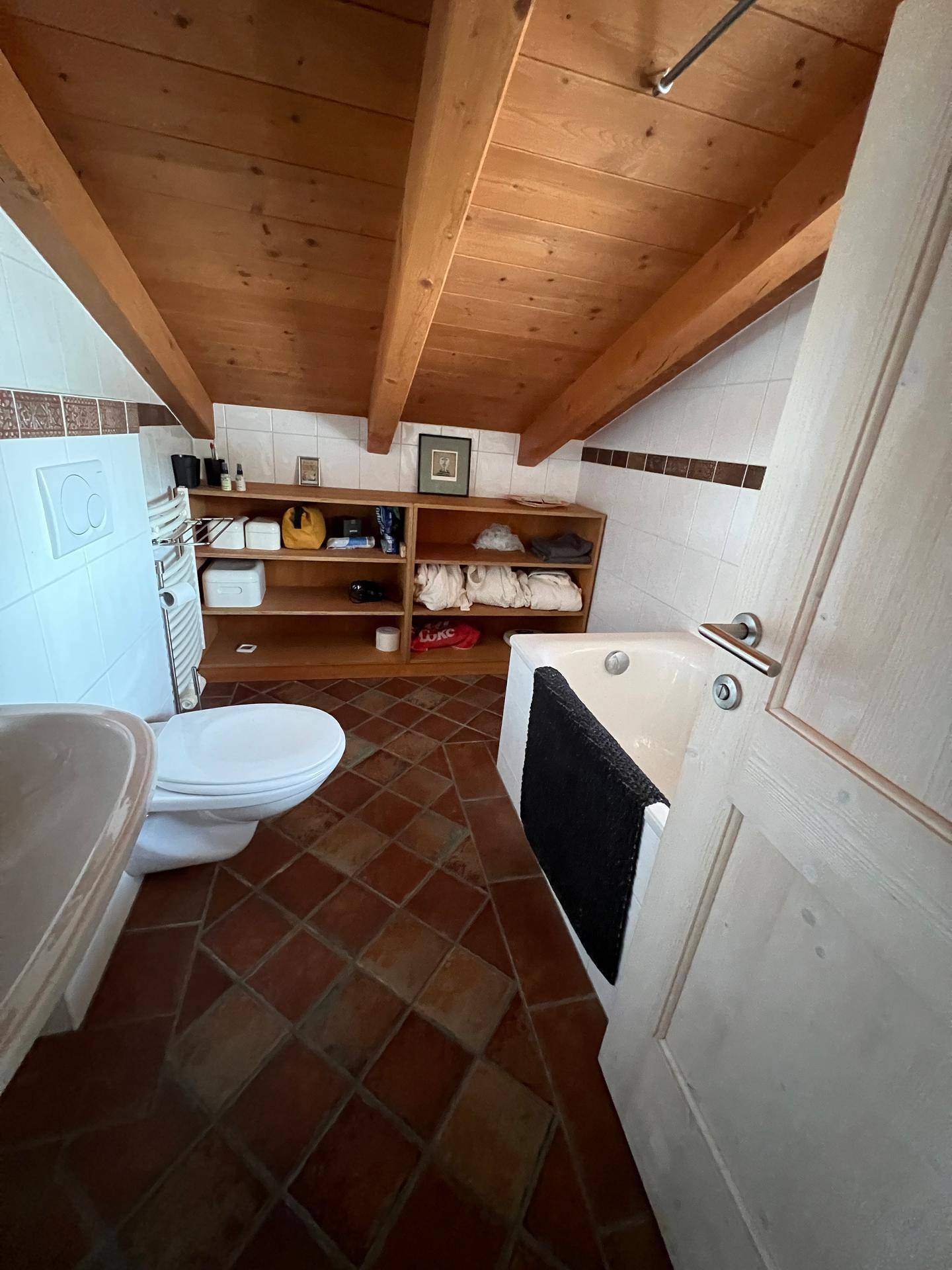 Badezimmer im Dachgeschoss mit Badewanne, WC und Terrakotta-Boden.
