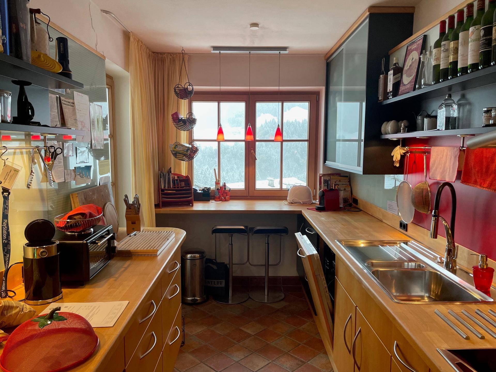 Funktionale Küche mit Holzarbeitsplatten, Terracotta-Boden und Fenster mit Bergblick.