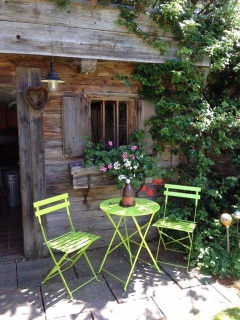 Gemütlicher Sitzbereich im Freien mit grünen Gartenmöbeln neben einer rustikalen Holzwand.
