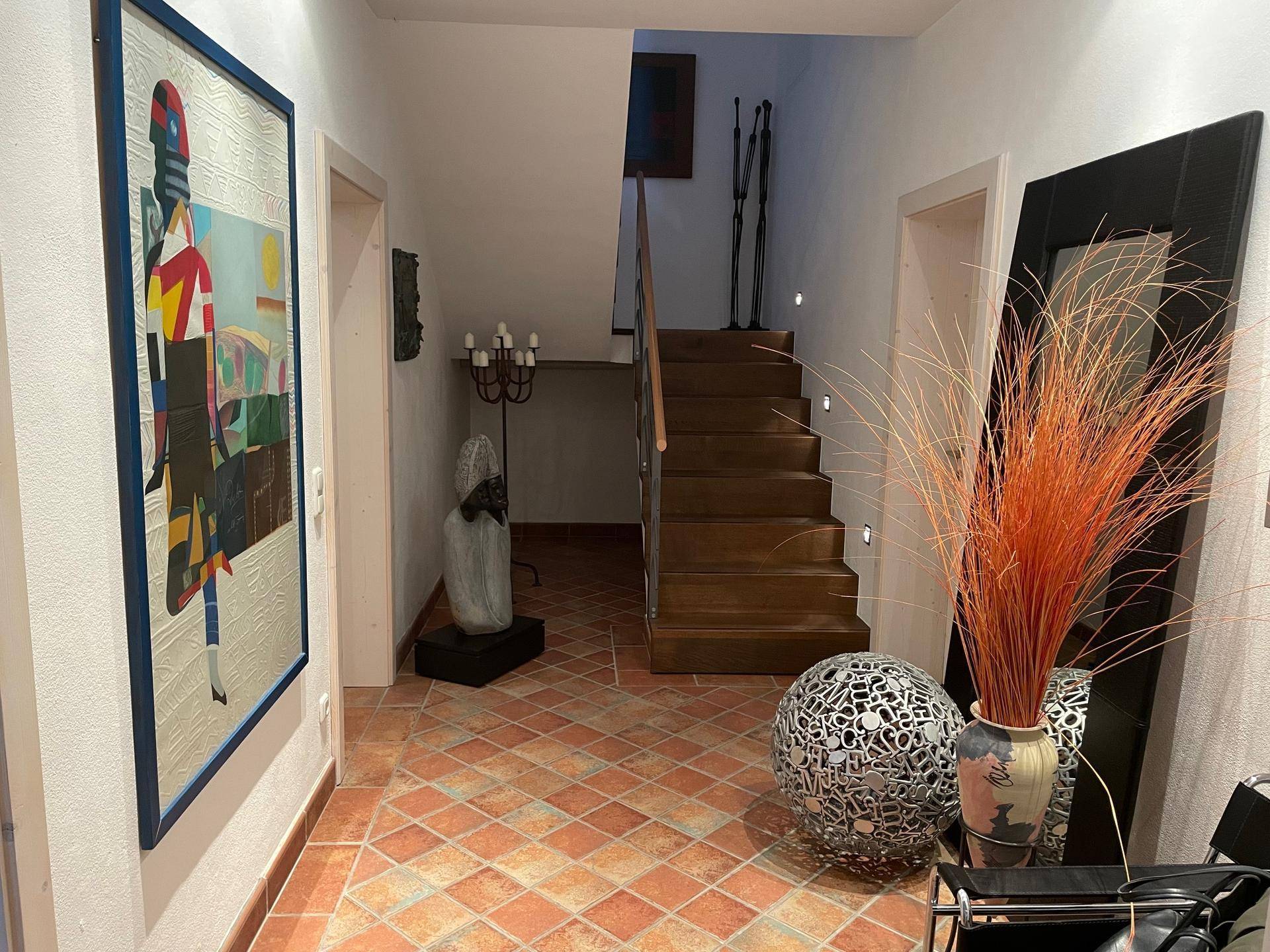 Geräumiger Flur mit Terrakotta-Boden, Treppe und moderner Kunstdekoration.