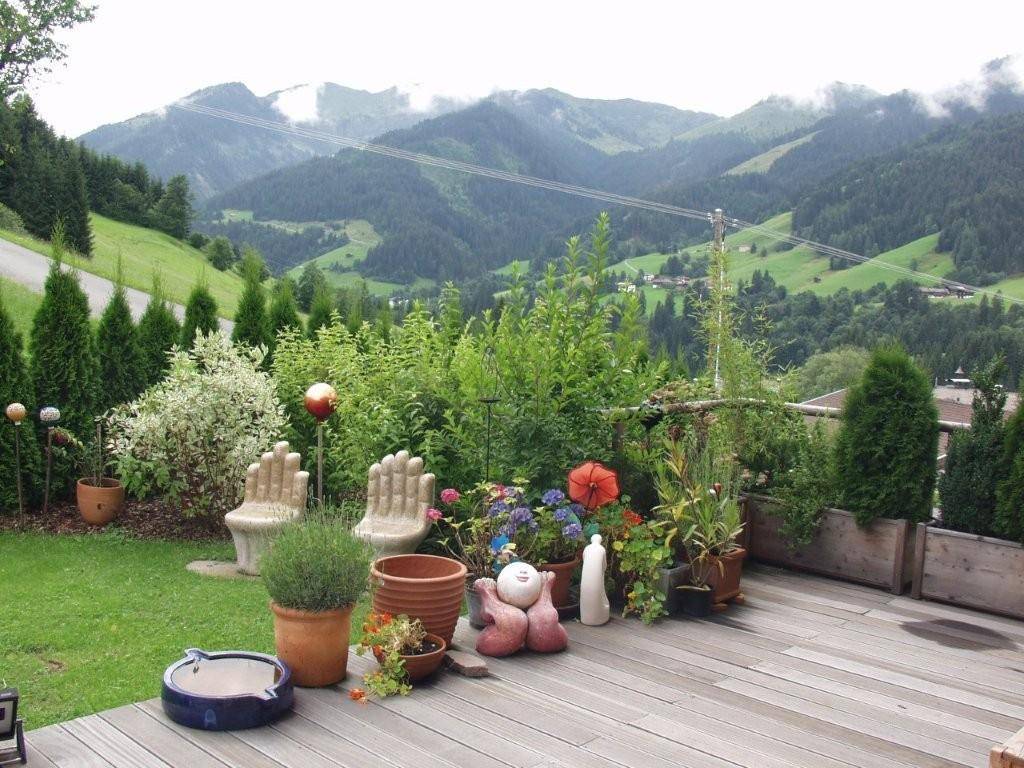 Sonnige Holzterrasse mit üppigem Garten und beeindruckendem Blick auf die grünen Berge.