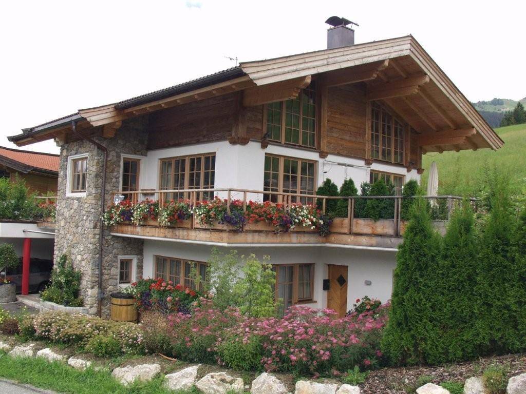 Charmantes Haus im alpinen Stil mit Holzbalkonen, Steinfassade und blühenden Blumenkästen.