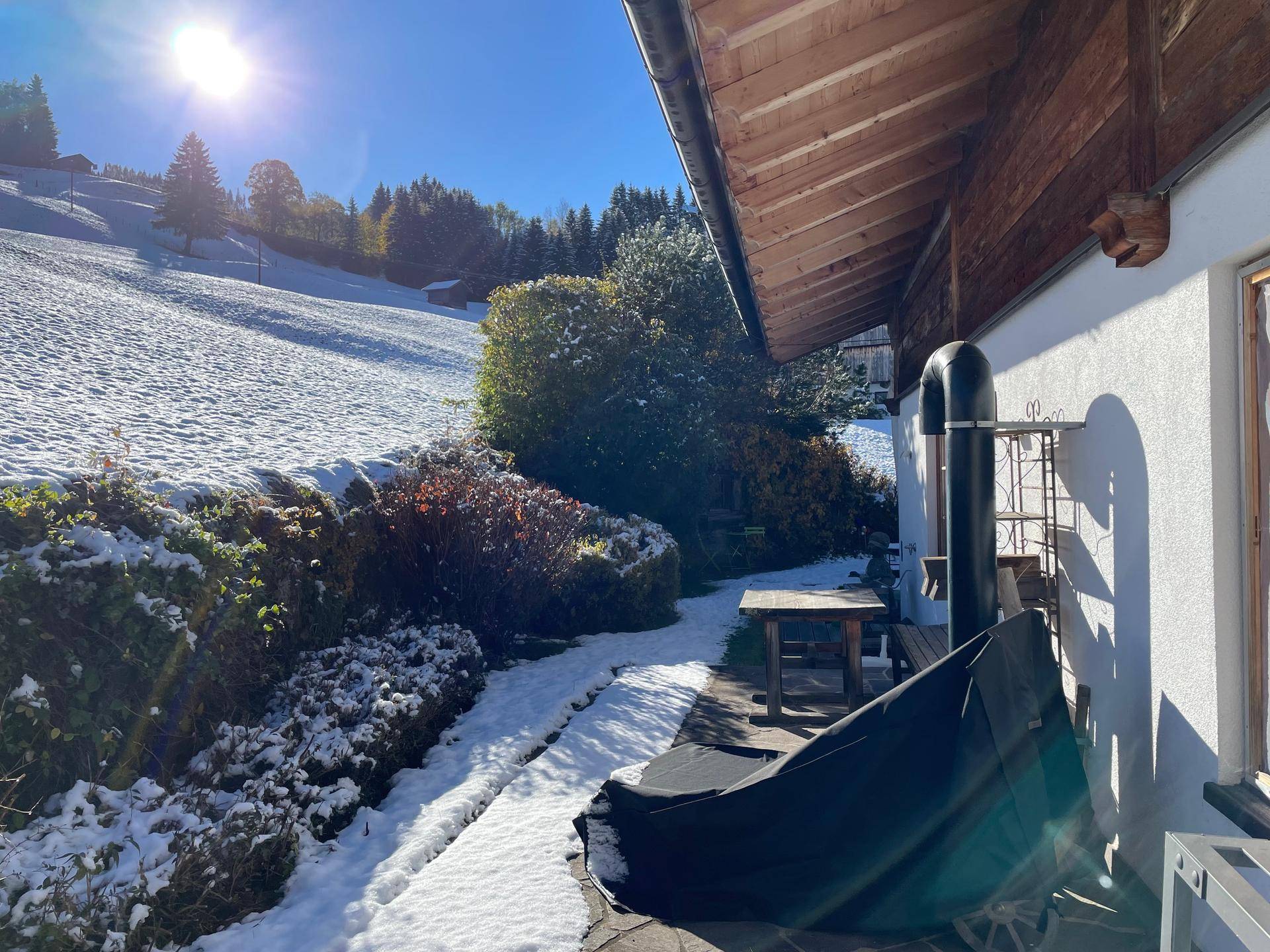 Gemütliche Terrasse mit Holztisch und Stühlen, umgeben von Schnee und Blick auf die Landschaft.