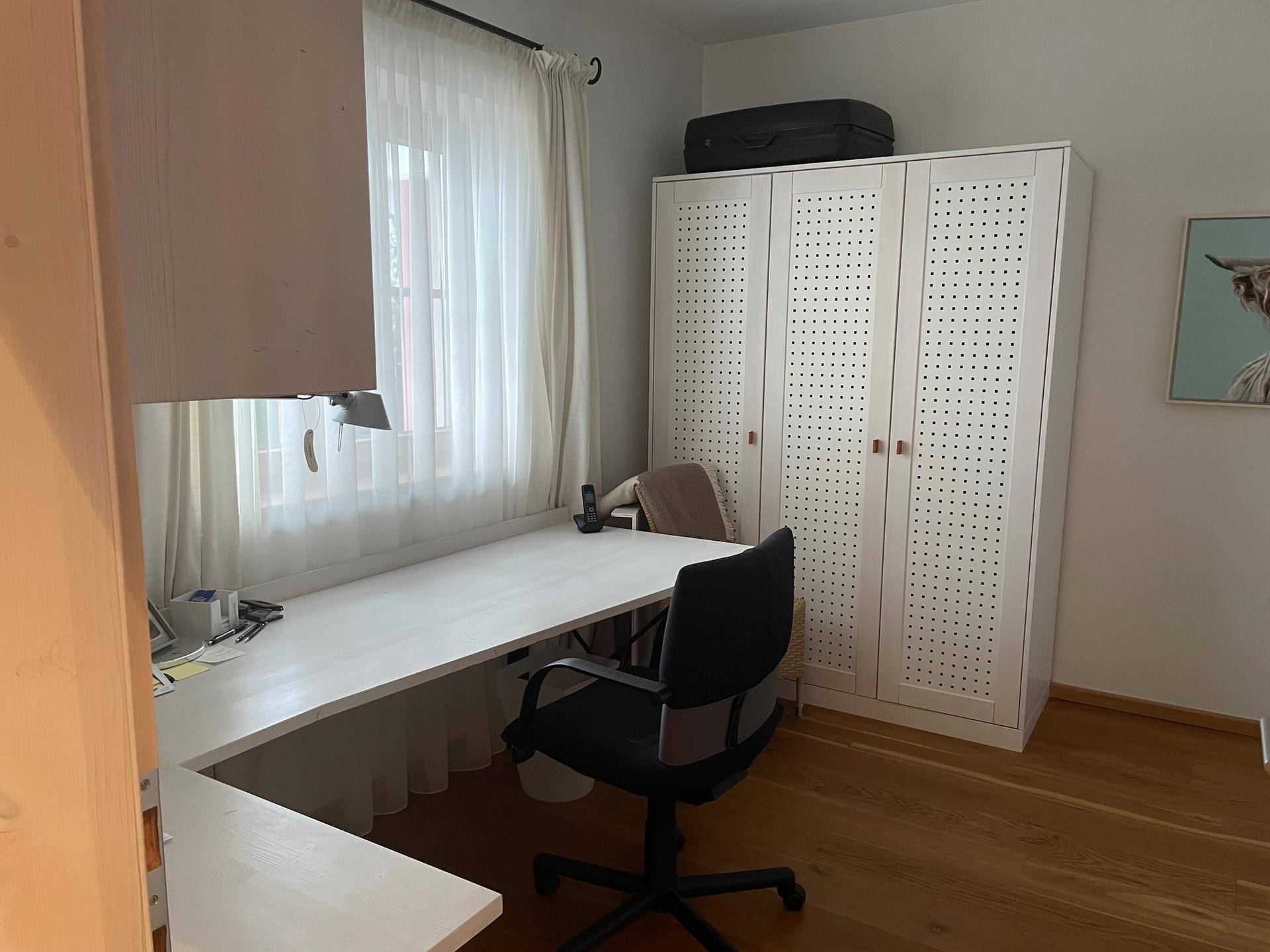 Helles Arbeitszimmer mit Schreibtisch, Schrank und Fenster mit Blick ins Grüne.
