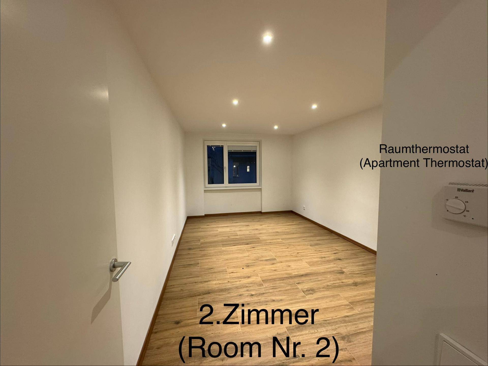 Helles Zimmer mit Holzboden, weißen Wänden und einem Fenster mit Thermostat.