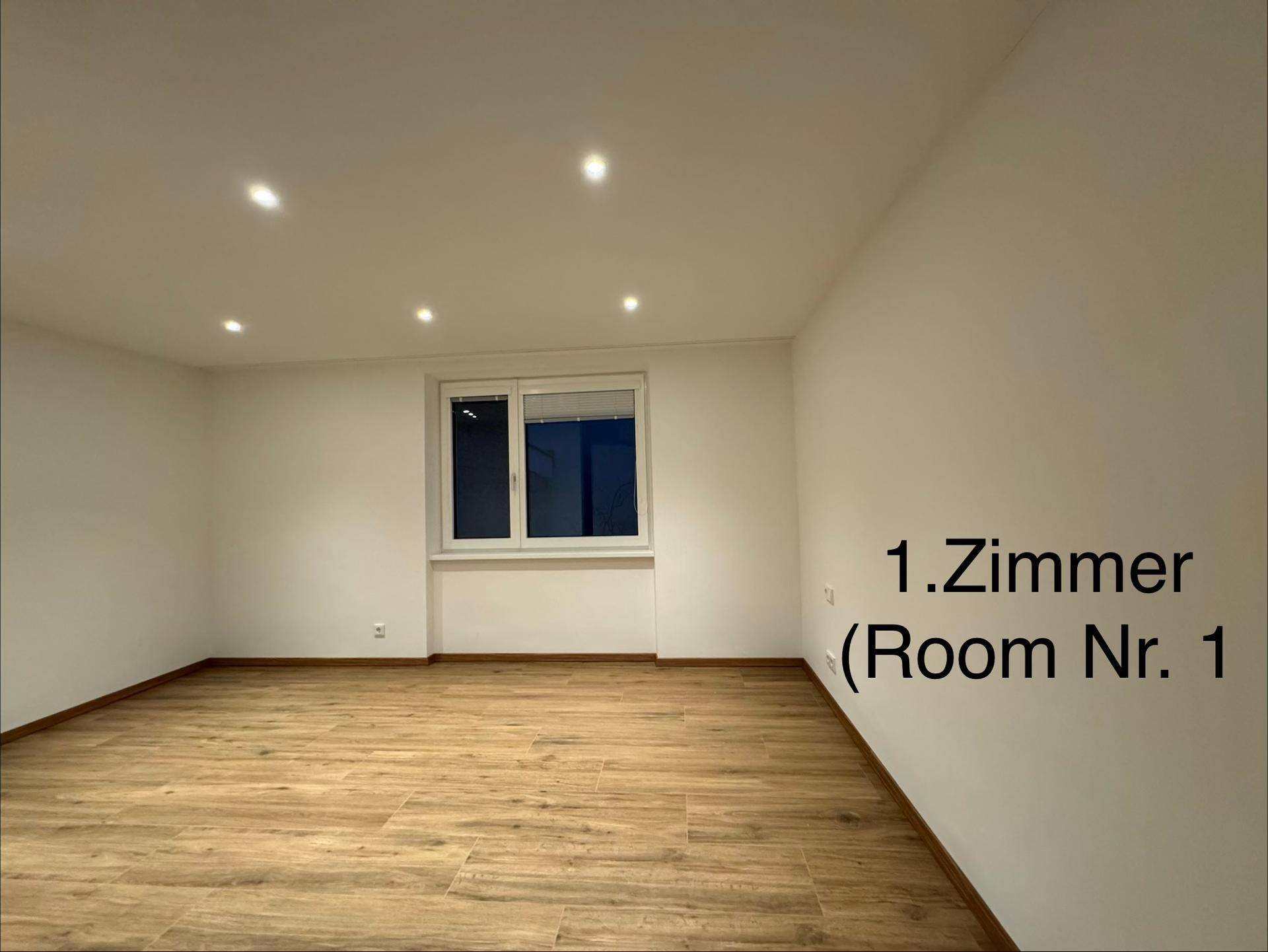 Helles Zimmer mit Holzboden, weißen Wänden und einem Fenster.