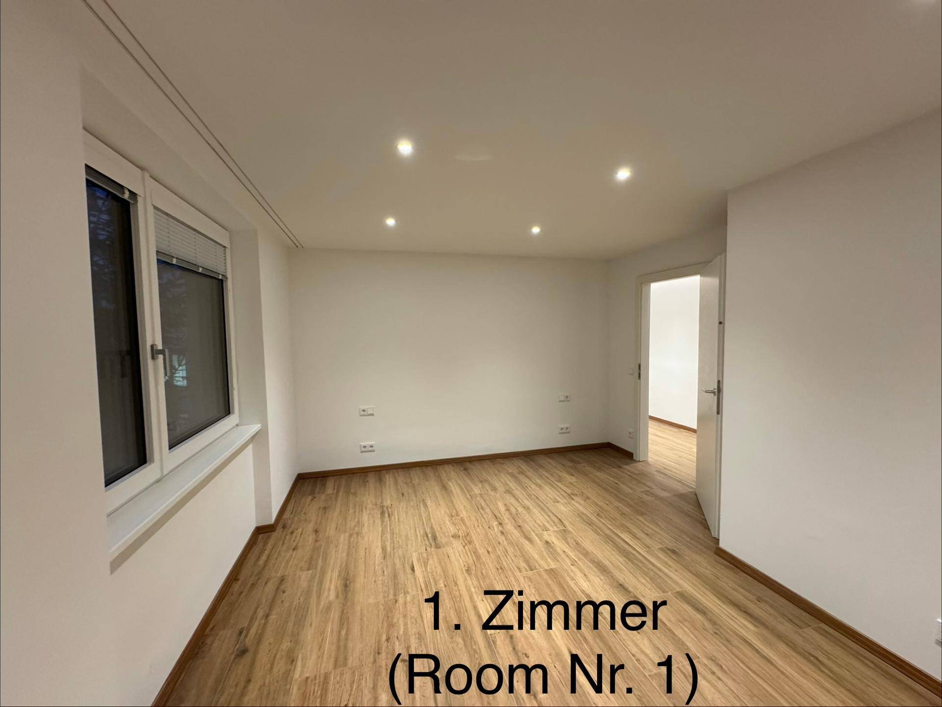 Geräumiges Zimmer mit Holzboden, weißen Wänden und mehreren Fenstern.
