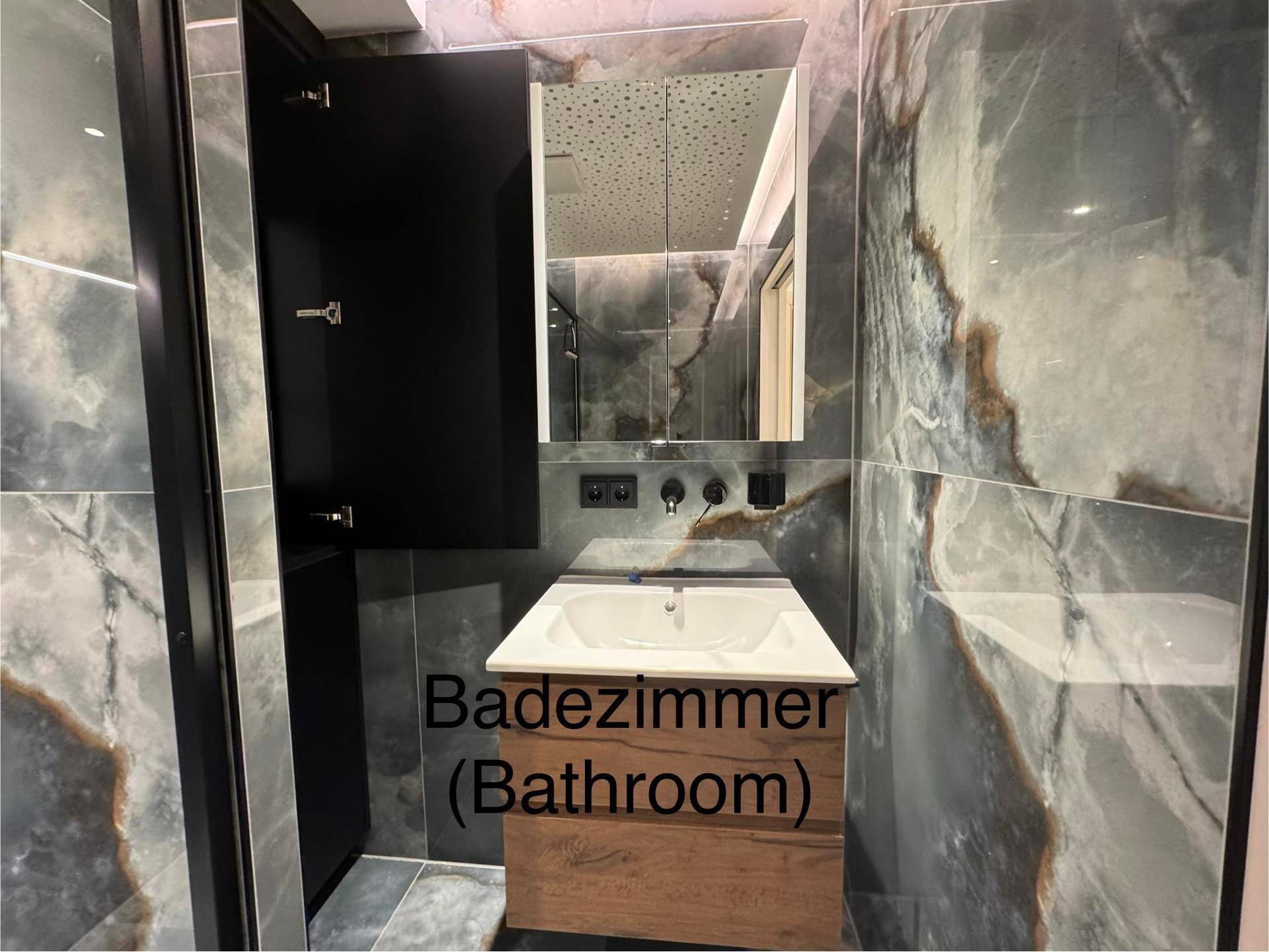 Modernes Badezimmer mit Waschtisch, Spiegel und großformatigen Fliesen in Marmoroptik.